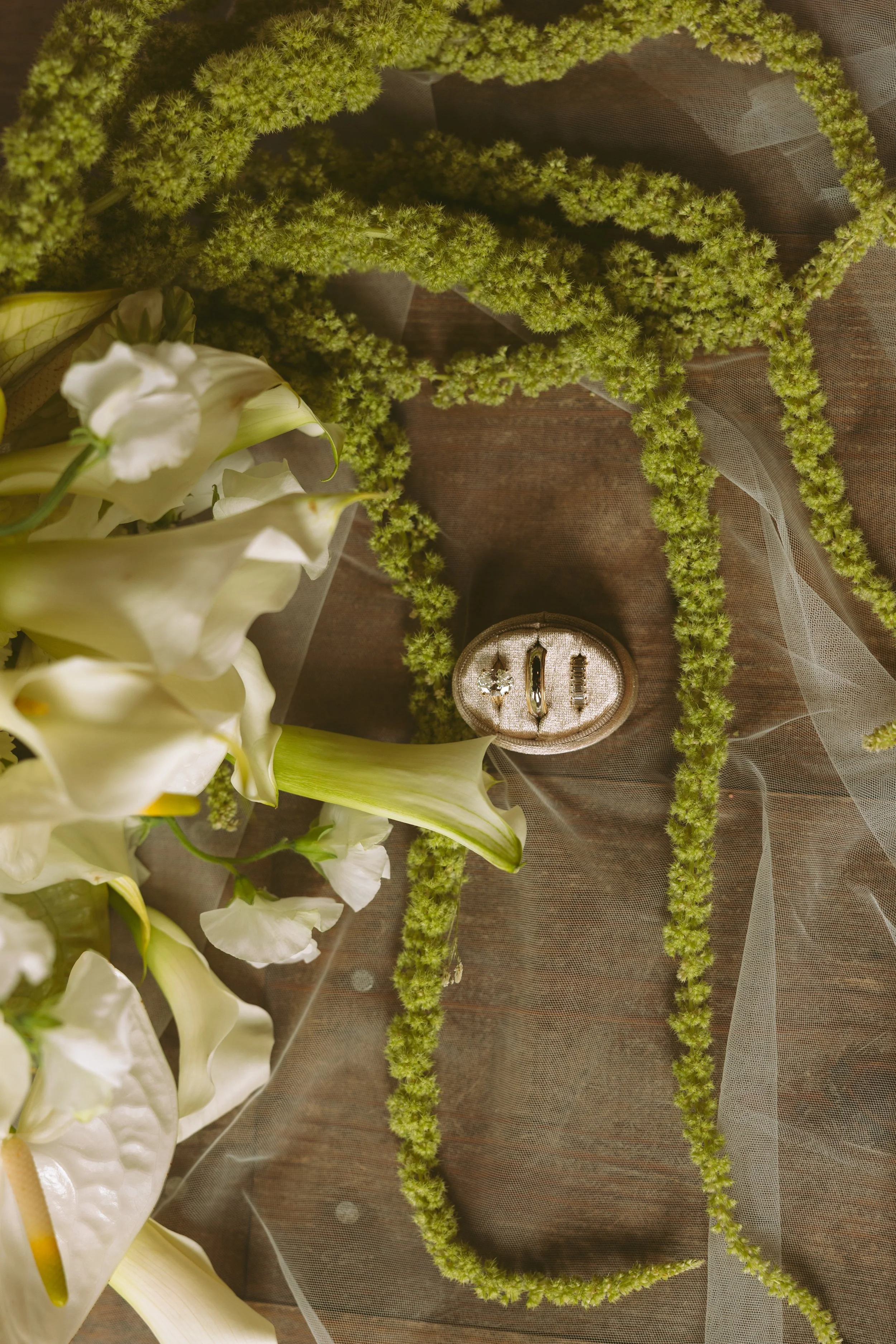 Arrangement of white flowers, including lilies and other blooms, with green trailing plants on a surface covered with sheer fabric.