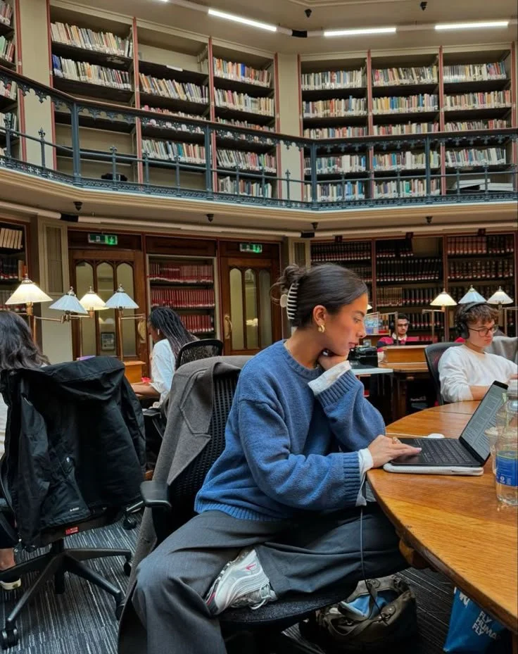 Menschen studieren in einer Bibliothek mit hohen Bücherregalen im Hintergrund.