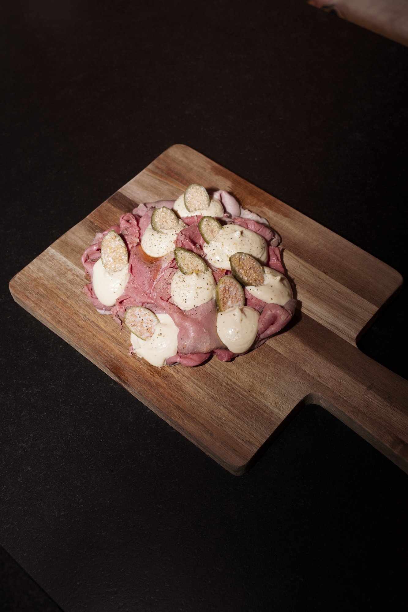 Sliced roast beef topped with creamy sauce and pickled vegetables on a wooden cutting board
