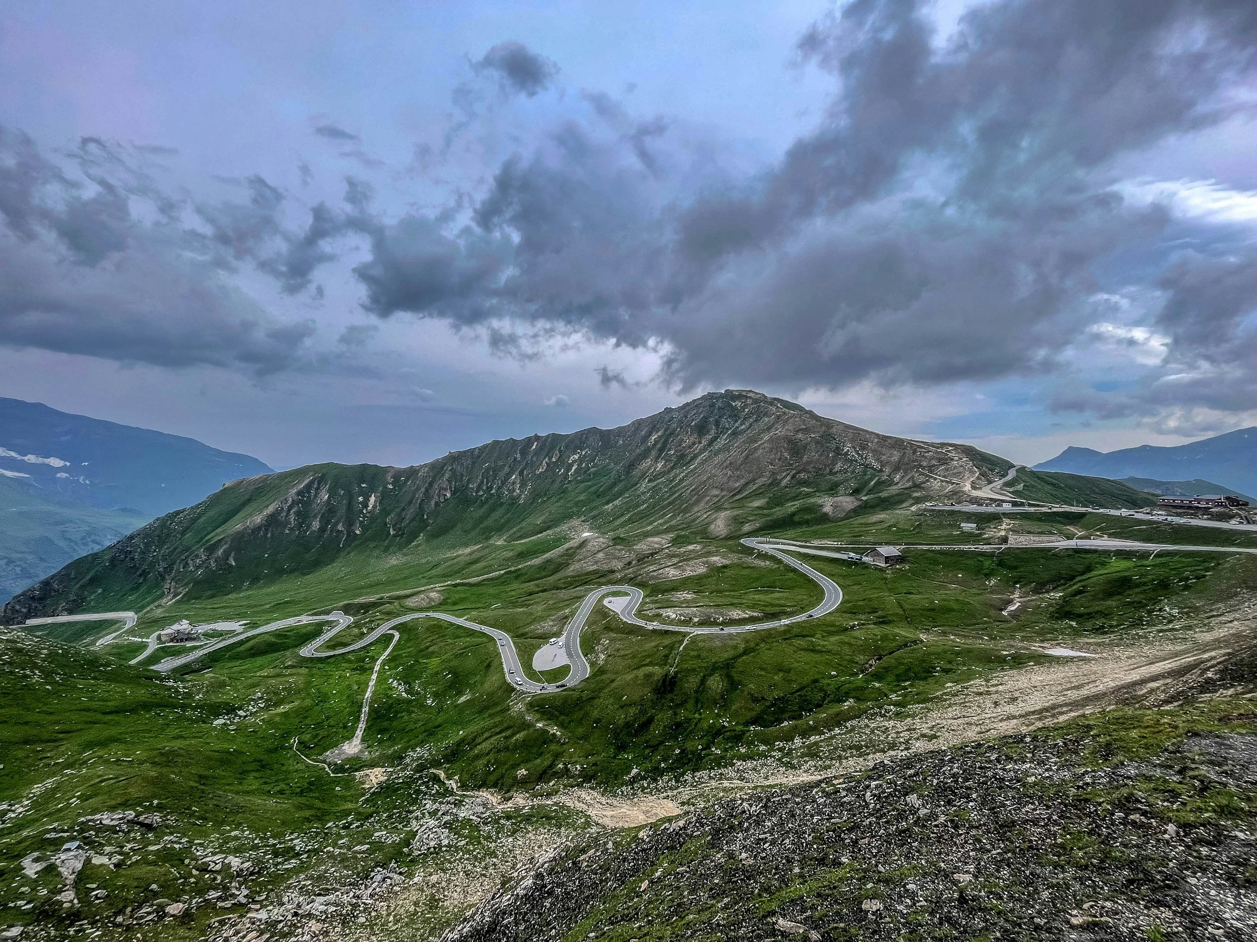 Mountain landscape with winding roads, green hills, and cloudy sky.