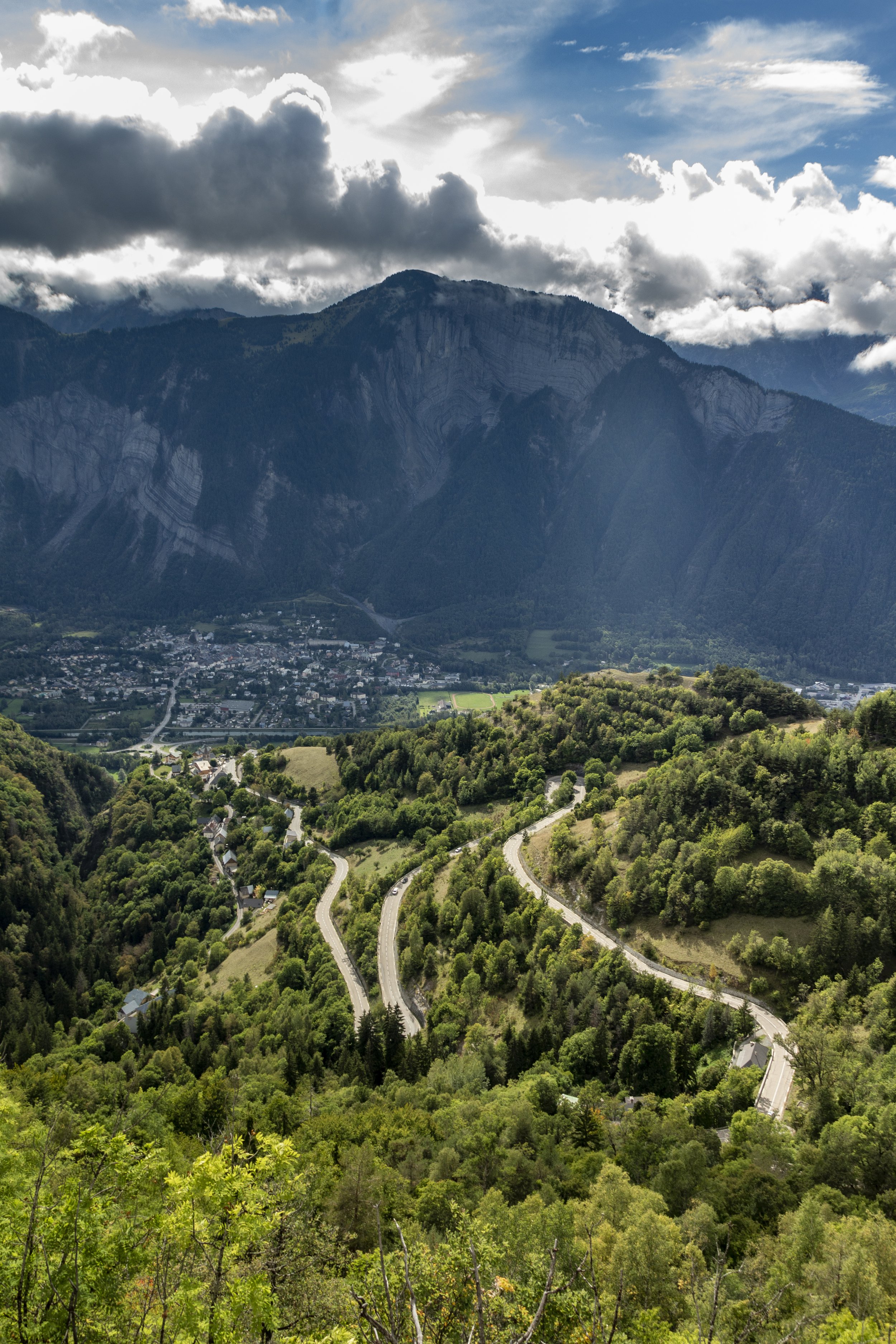 Winding road through lush green forest with mountains and cloudy sky in the background