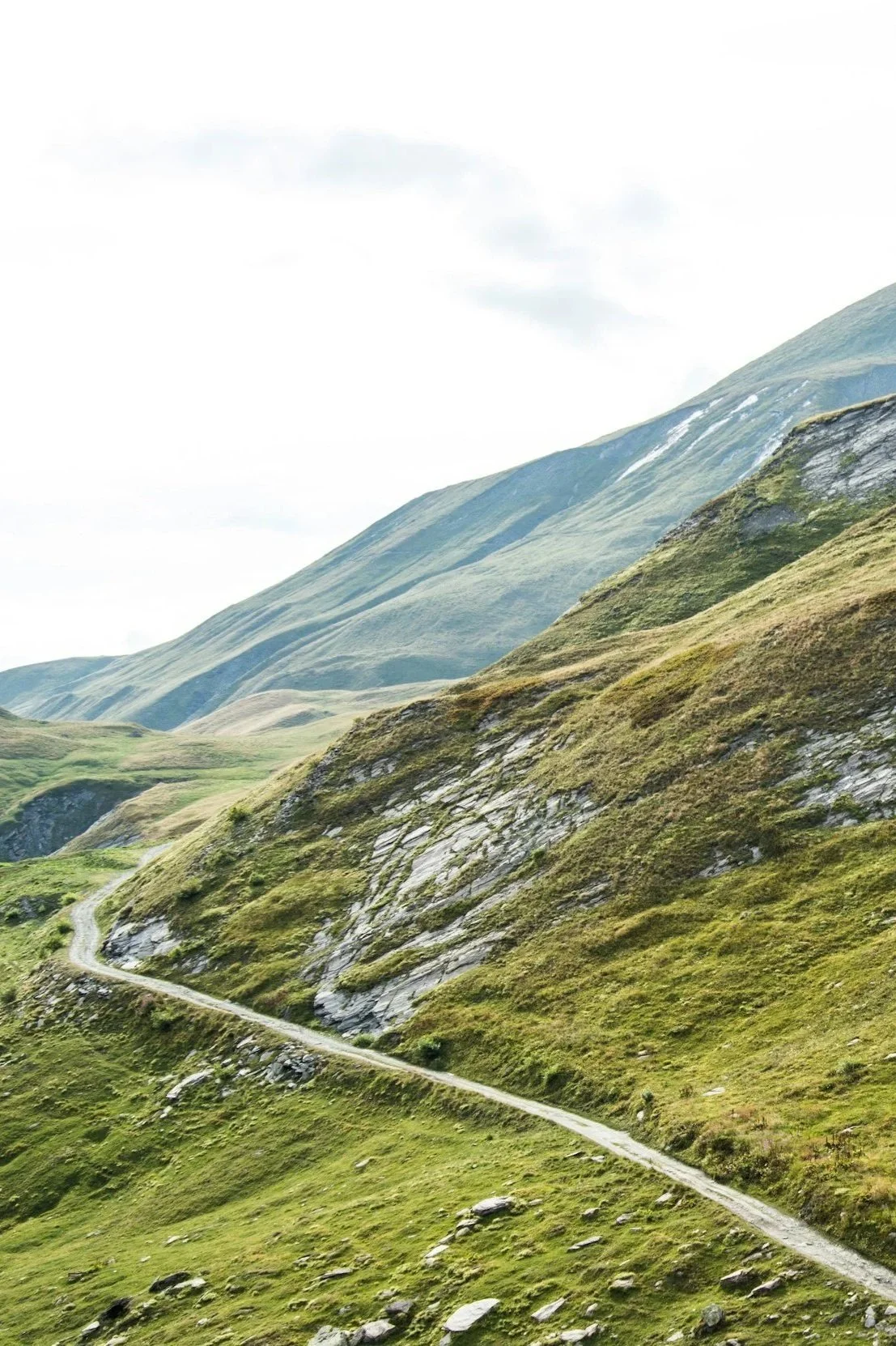 Mountain landscape with green hills and a winding dirt road.