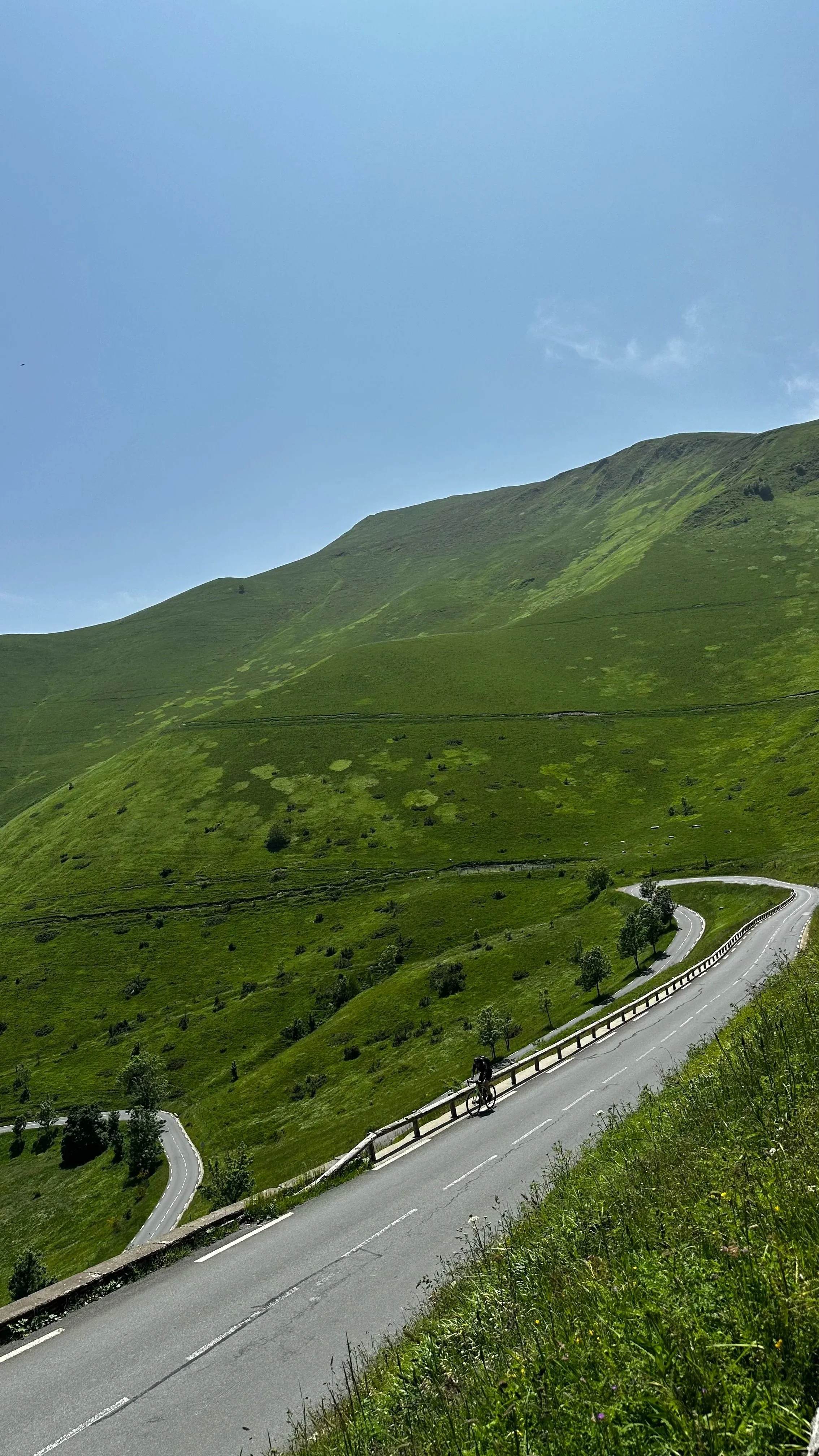 A winding mountainous road in lush green hills with a cyclist riding along.
