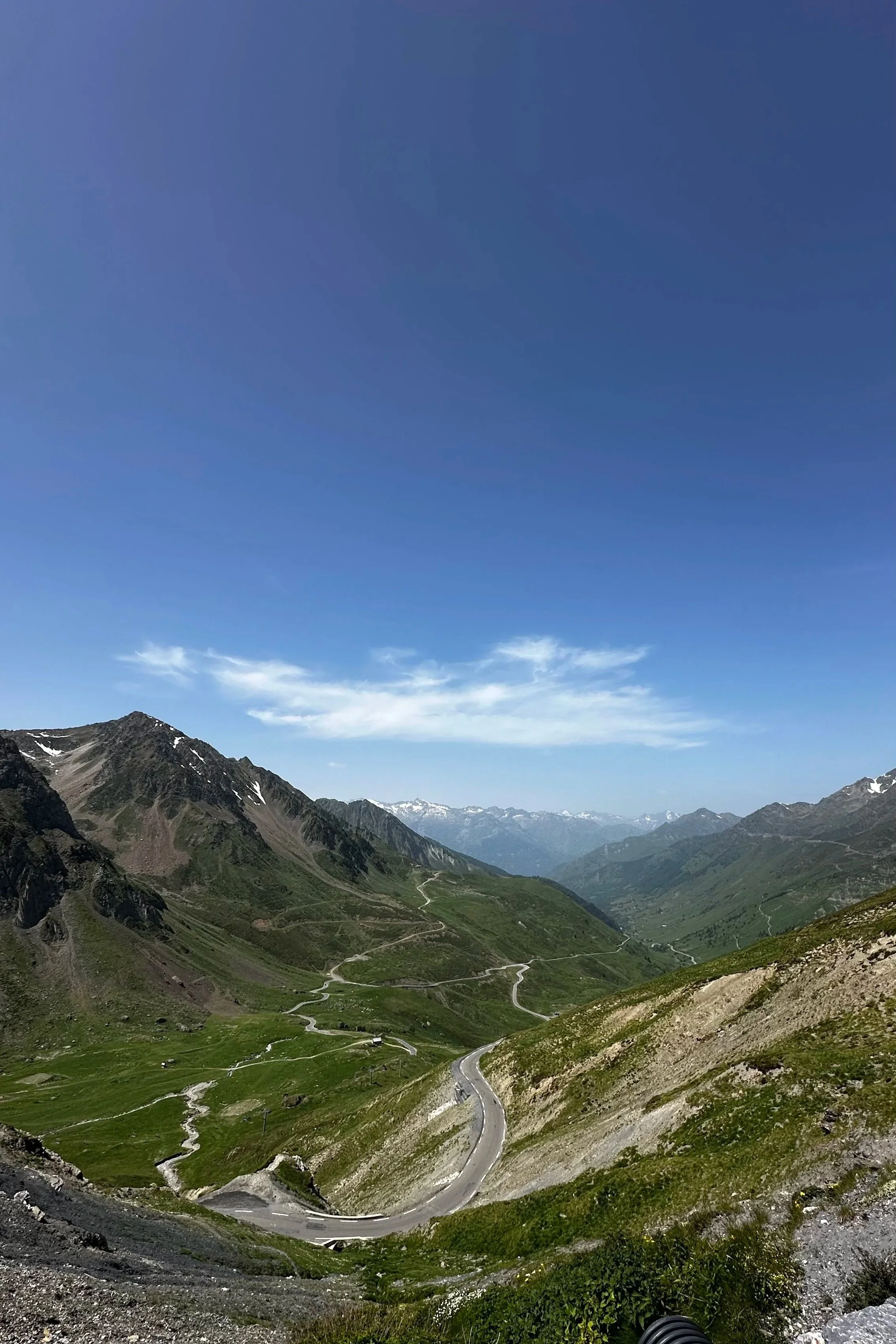 Mountain range with winding road and green valleys under a clear blue sky.