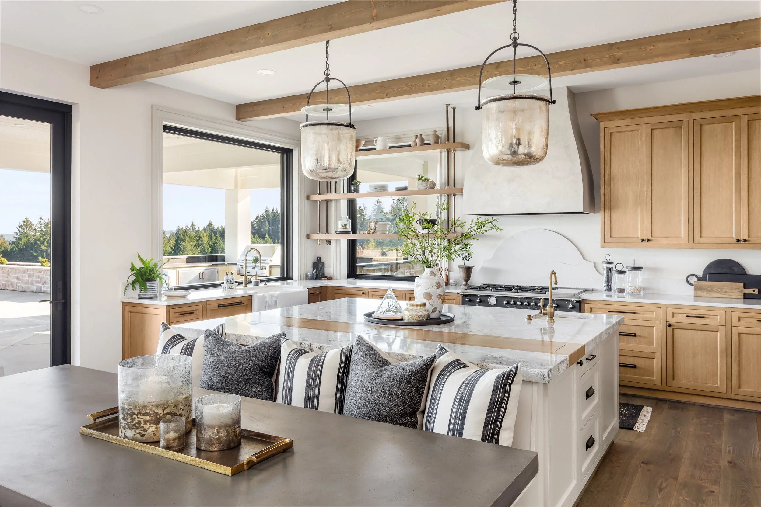 Modern kitchen with wooden cabinets, open shelves, large windows, and a central island with decorative vases and greenery.