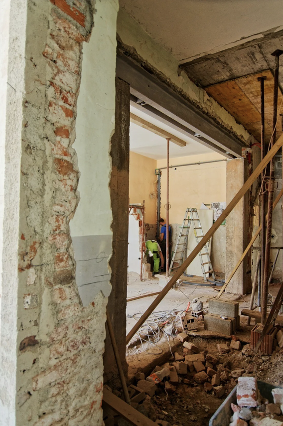 Construction workers remodeling an interior space with exposed brick walls, scaffolding, and partial demolition.