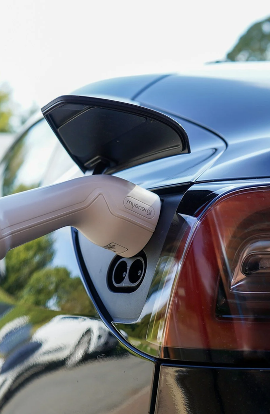 Electric vehicle charging port with a charging cable connected to a car in an outdoor setting.