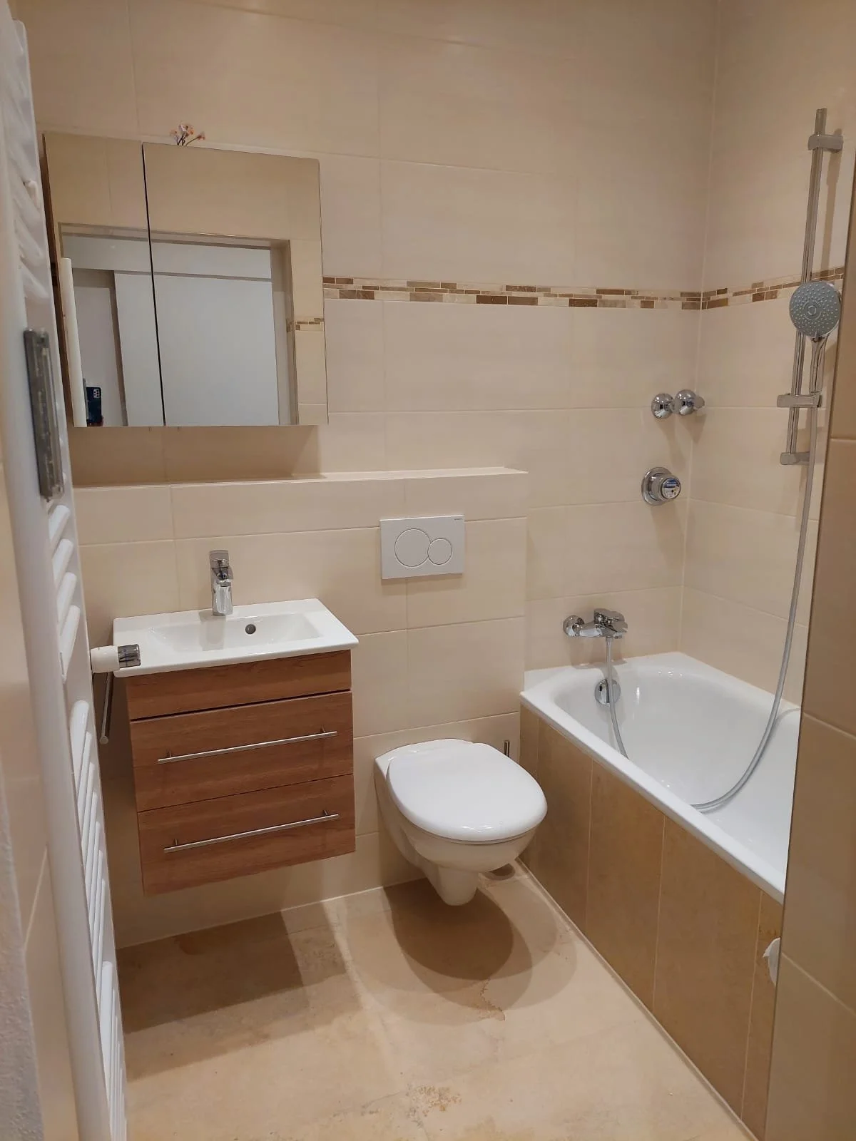 Ein Badezimmer mit Waschbecken, Toilette, Badewanne, Wandspiegel und Handtuchheizkörper, in neutralen Beige- und Brauntönen gehalten.