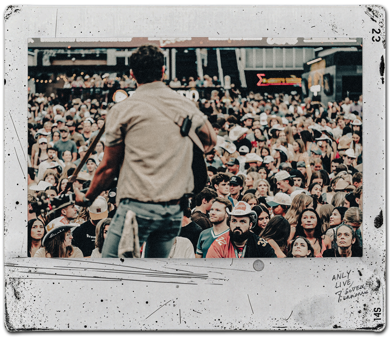 A man with a guitar performs in front of a large crowd at a concert or festival.