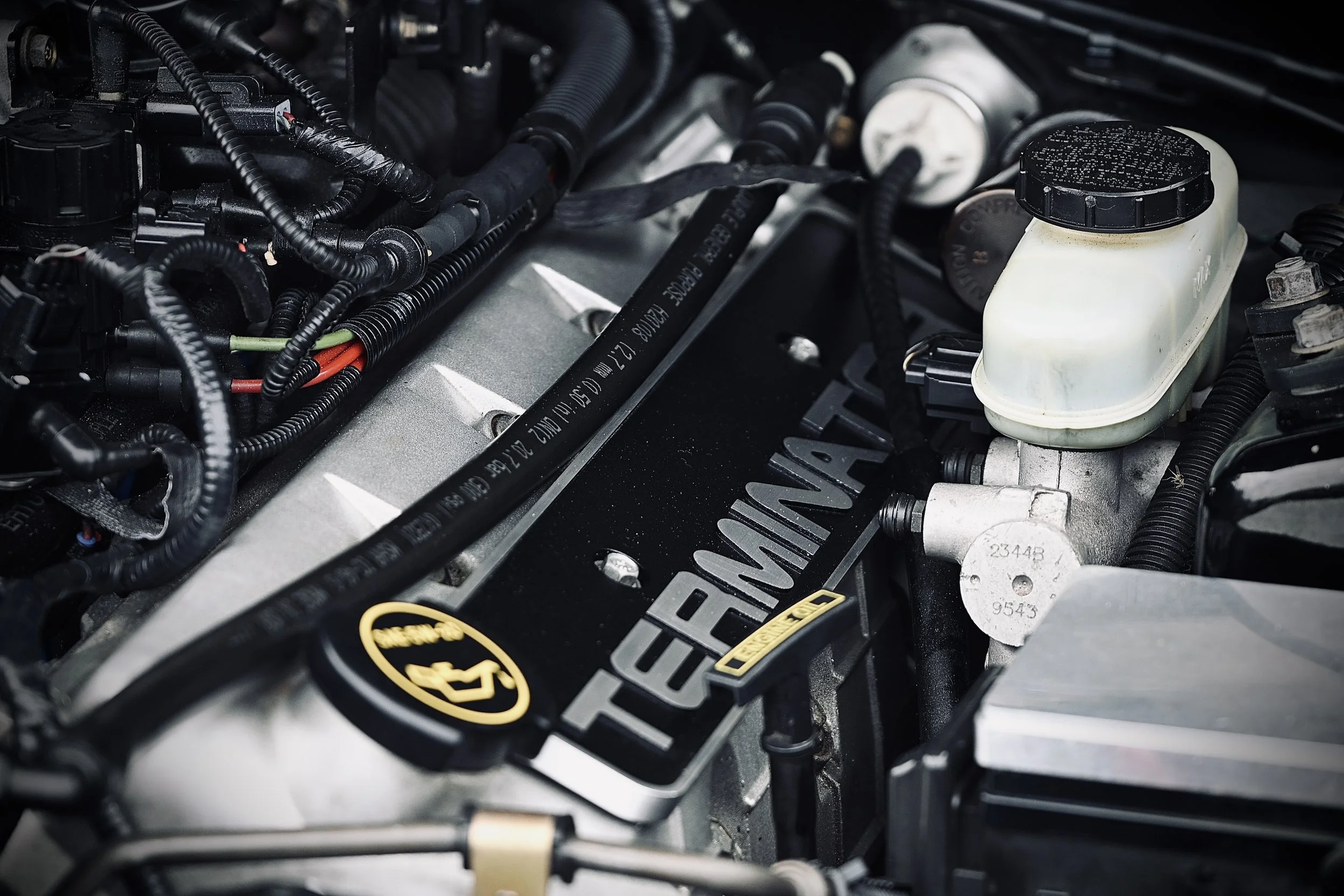 Close-up of a car engine showcasing various hoses, wires, and components, including a white fluid reservoir and metal parts.