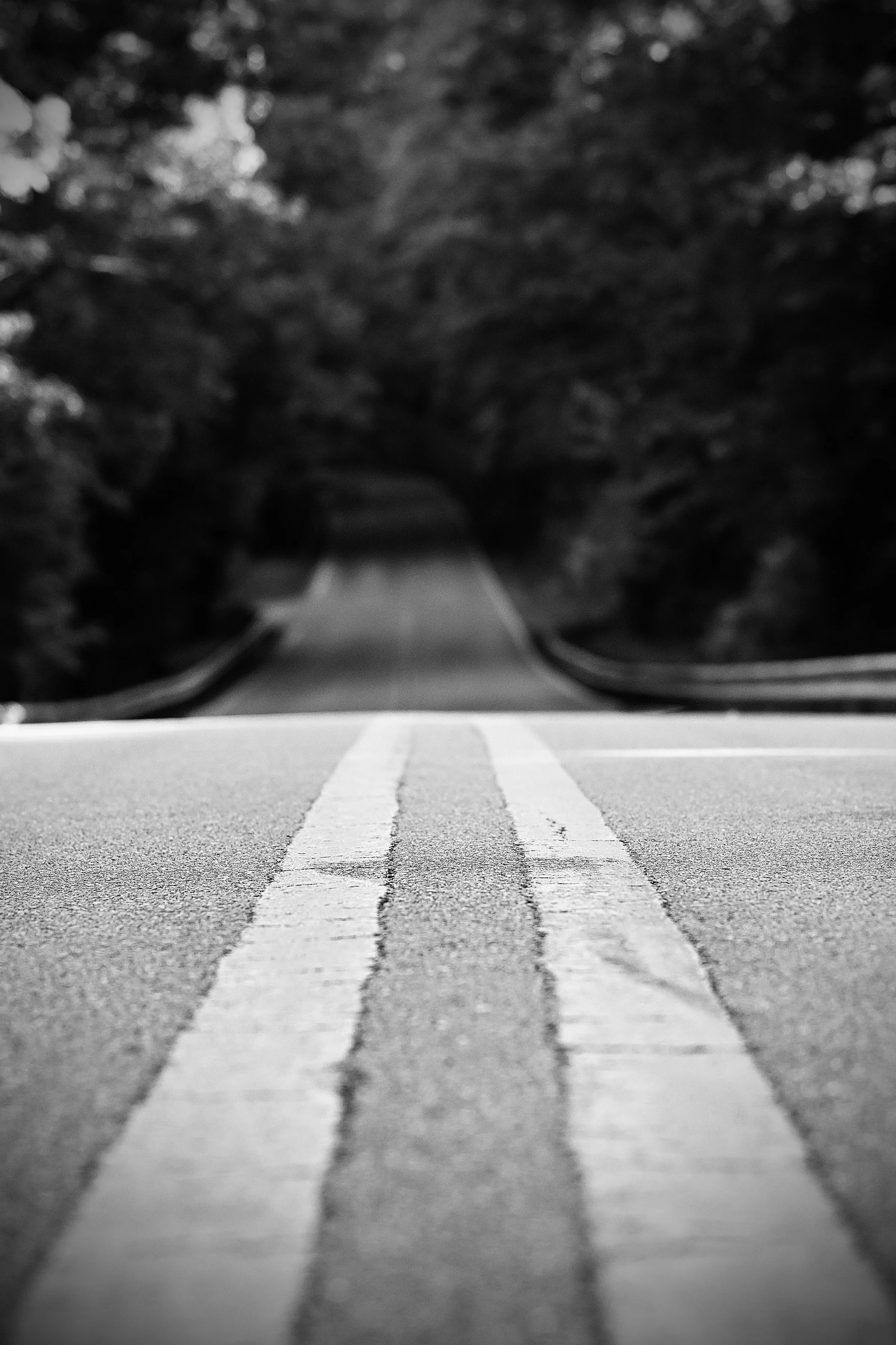 Black and white photograph of a road with two white lines, viewed from a very low angle, with a dark tunnel or underpass at the top of the image.