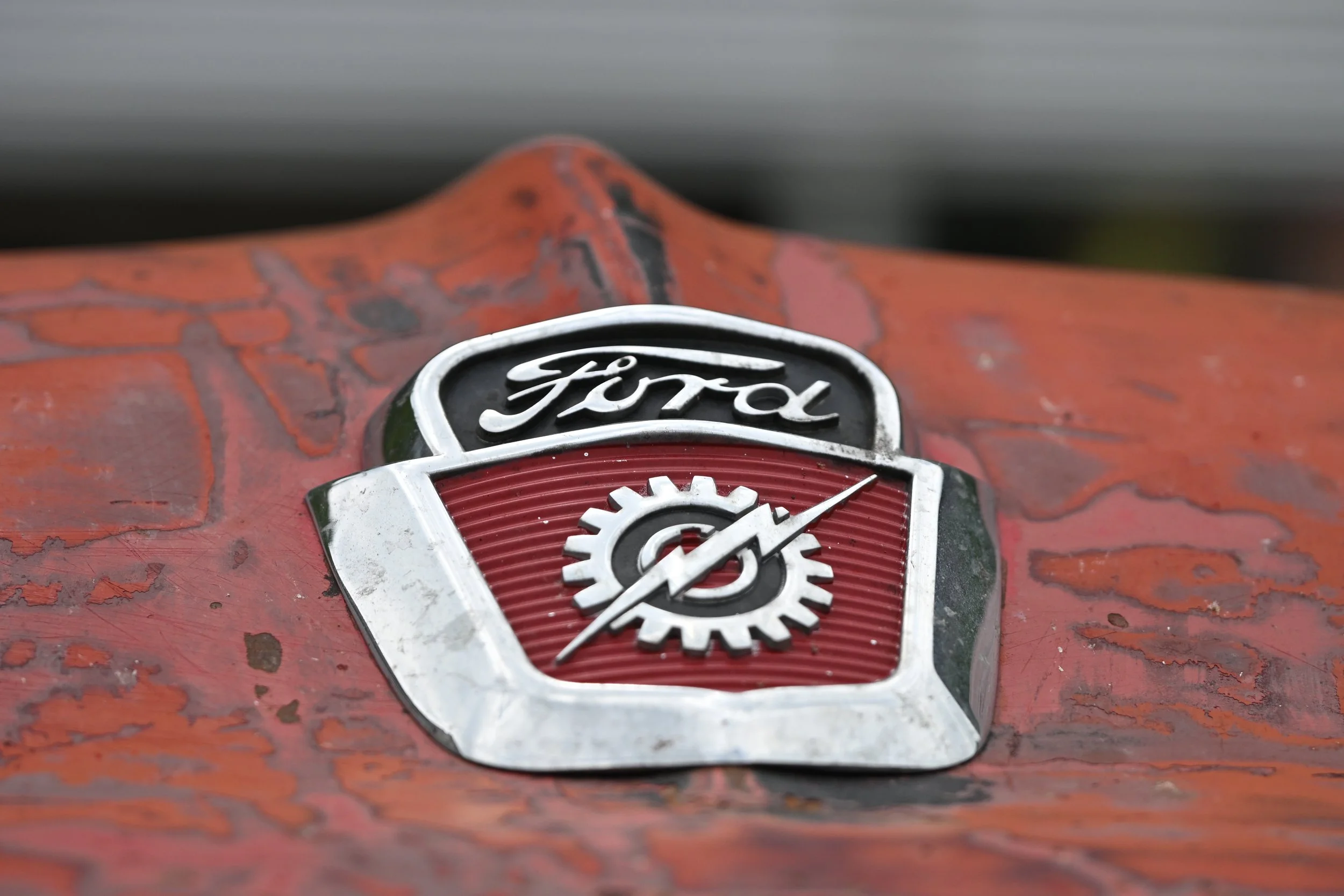 Close-up of a vintage Ford logo badge on a weathered red metal surface.