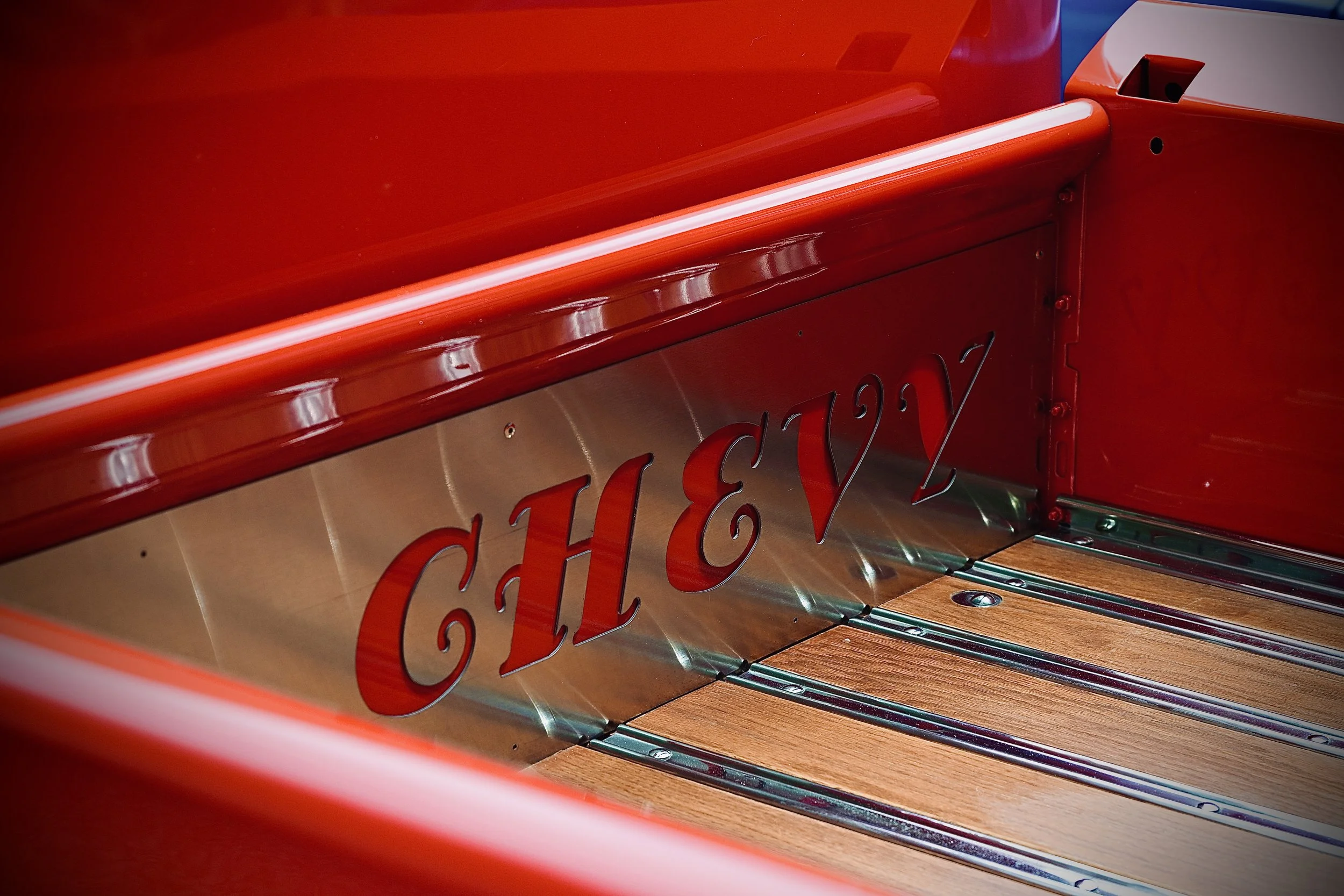 Close-up of a red truck bed showing some of the custom metal work with wooden panels.
