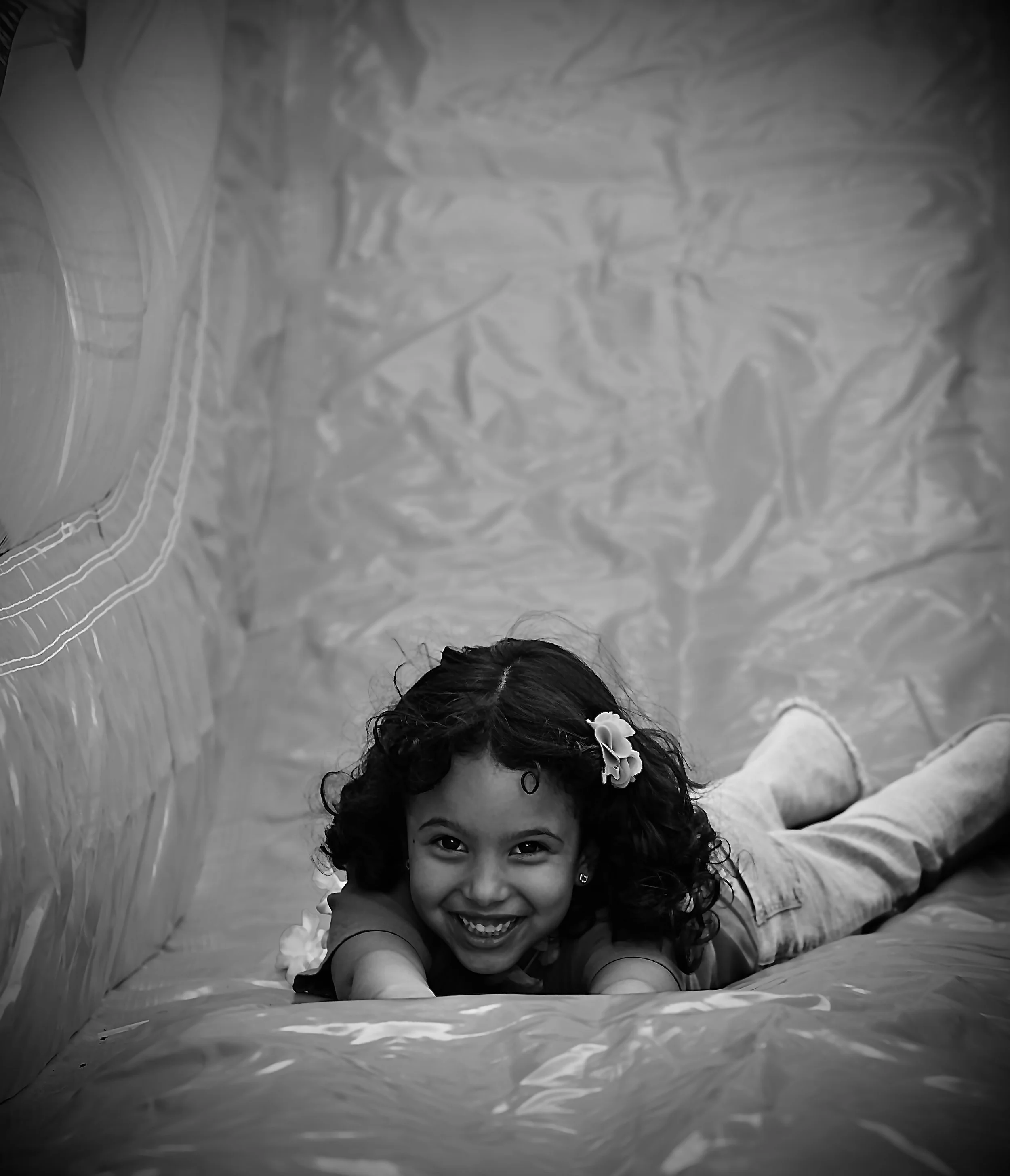A young girl on an inflatable surface, reaching out with her arms, with a background of inflated material.