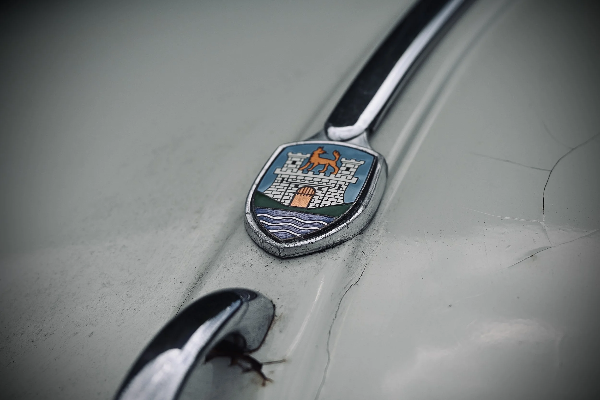 Close-up of a vintage car emblem with a lion and a castle, mounted on the car's hood.