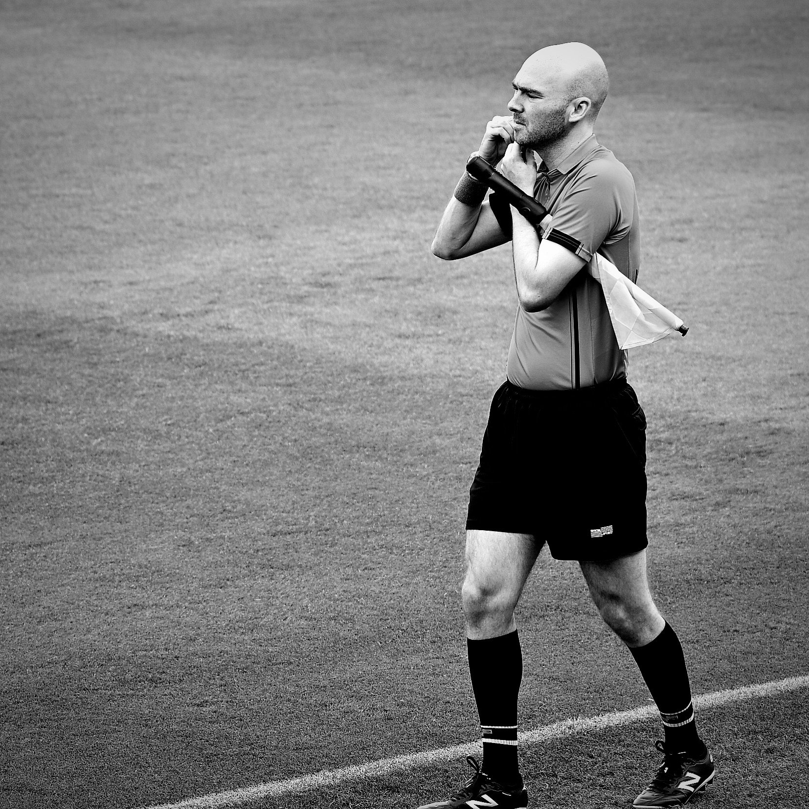 A bald man dressed in sports gear, including a short-sleeved shirt, shorts, and running shoes, standing on a grassy field with a determined or thoughtful expression, possibly during a sports event or practice.