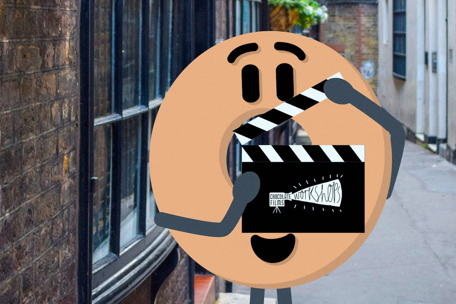 A cartoon-style emoticon character with a round face, holding a clapperboard labeled 'Chocolate Work Shop Films,' in an outdoor urban setting.