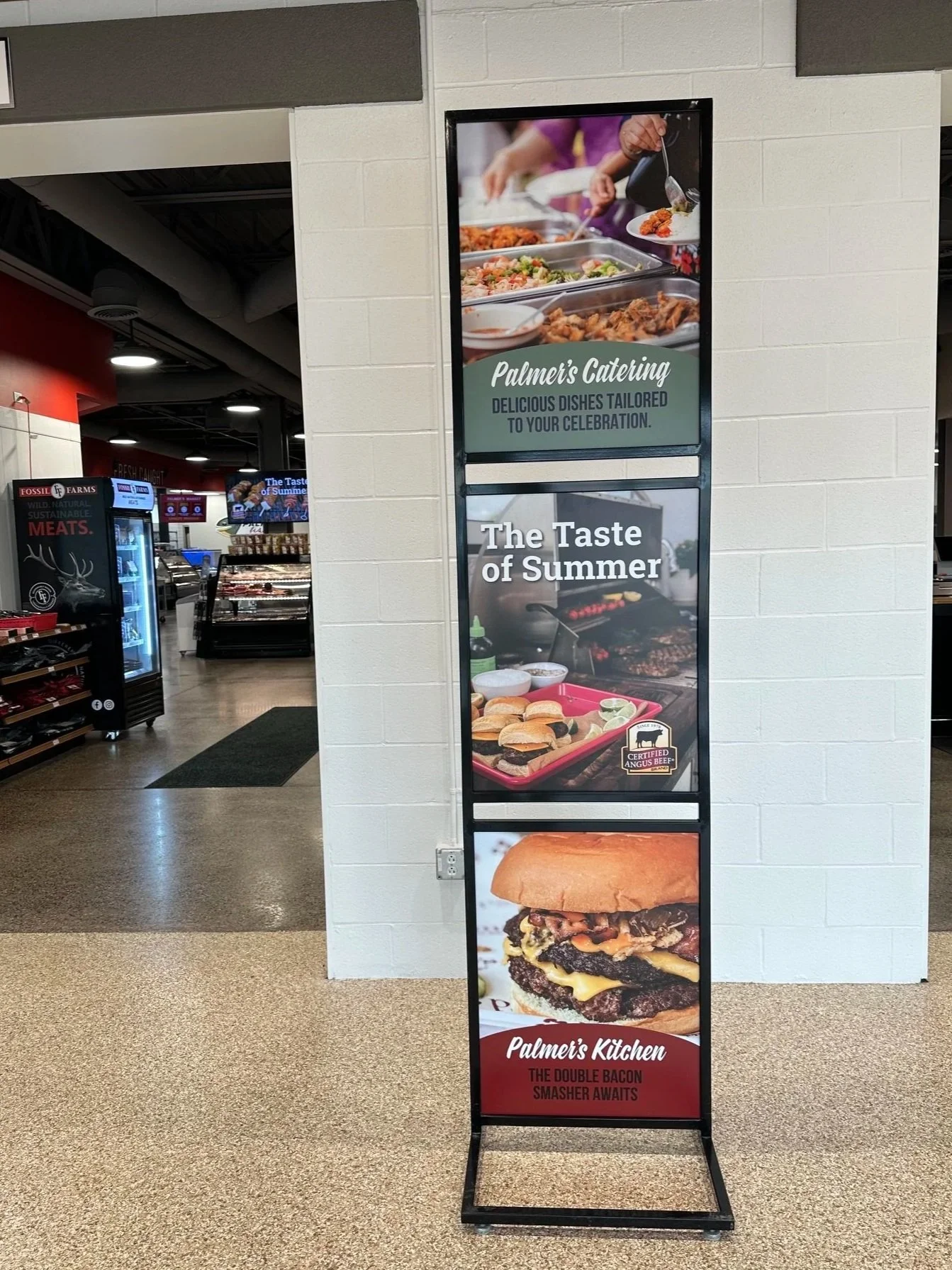 Vertical restaurant sign with images of food and text advertising Palmer's Catering and Palmer's Kitchen. The top part shows buffet trays, the middle features sandwiches, and the bottom showcases a burger with bacon and cheese.