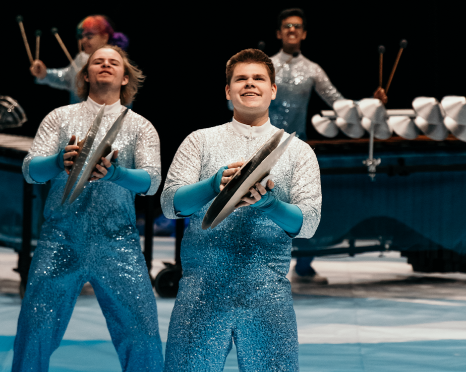 Four young performers in glittery blue costumes holding cymbals during a stage performance.