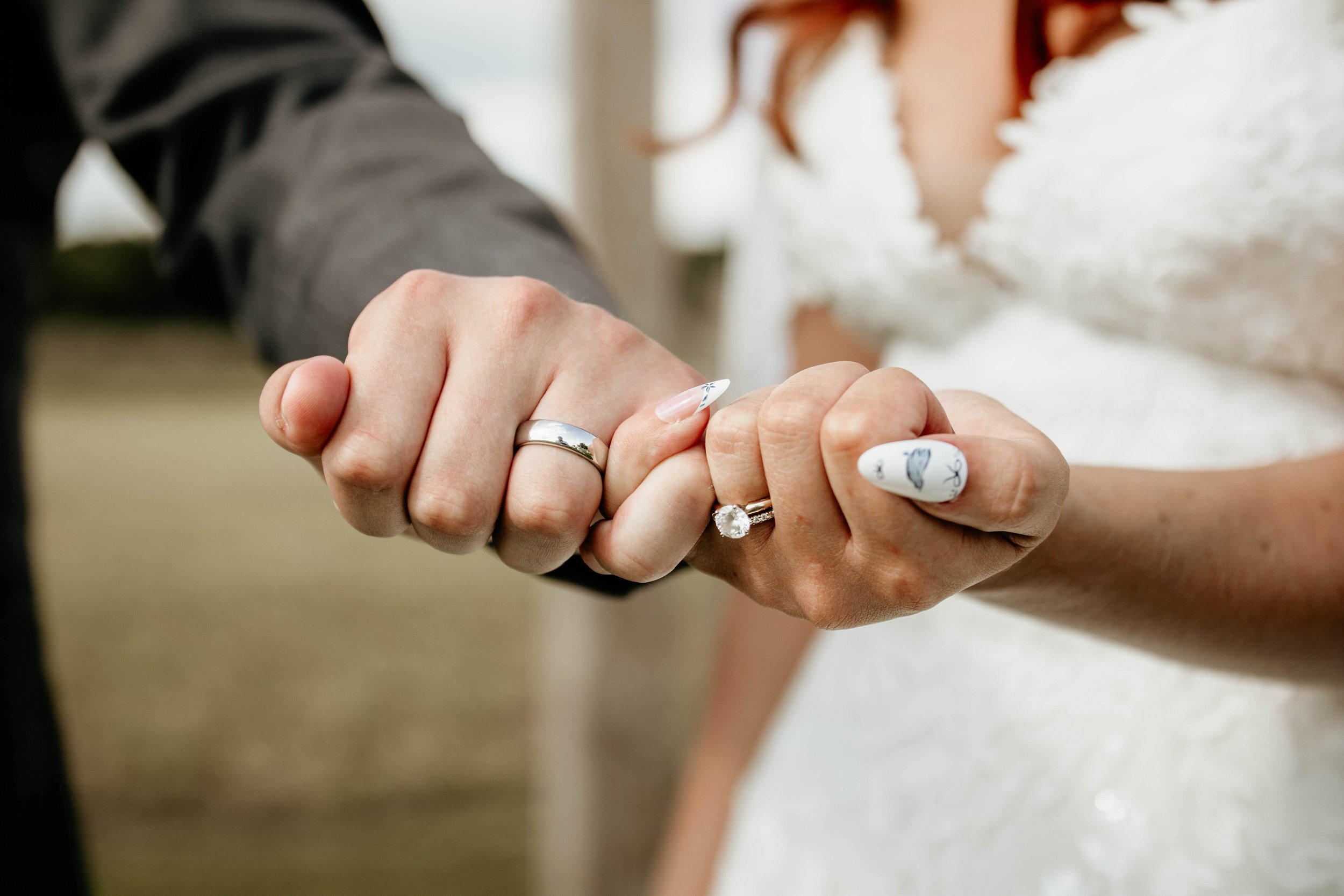 Close-up of a man and woman holding hands during their wedding, with wedding rings visible.