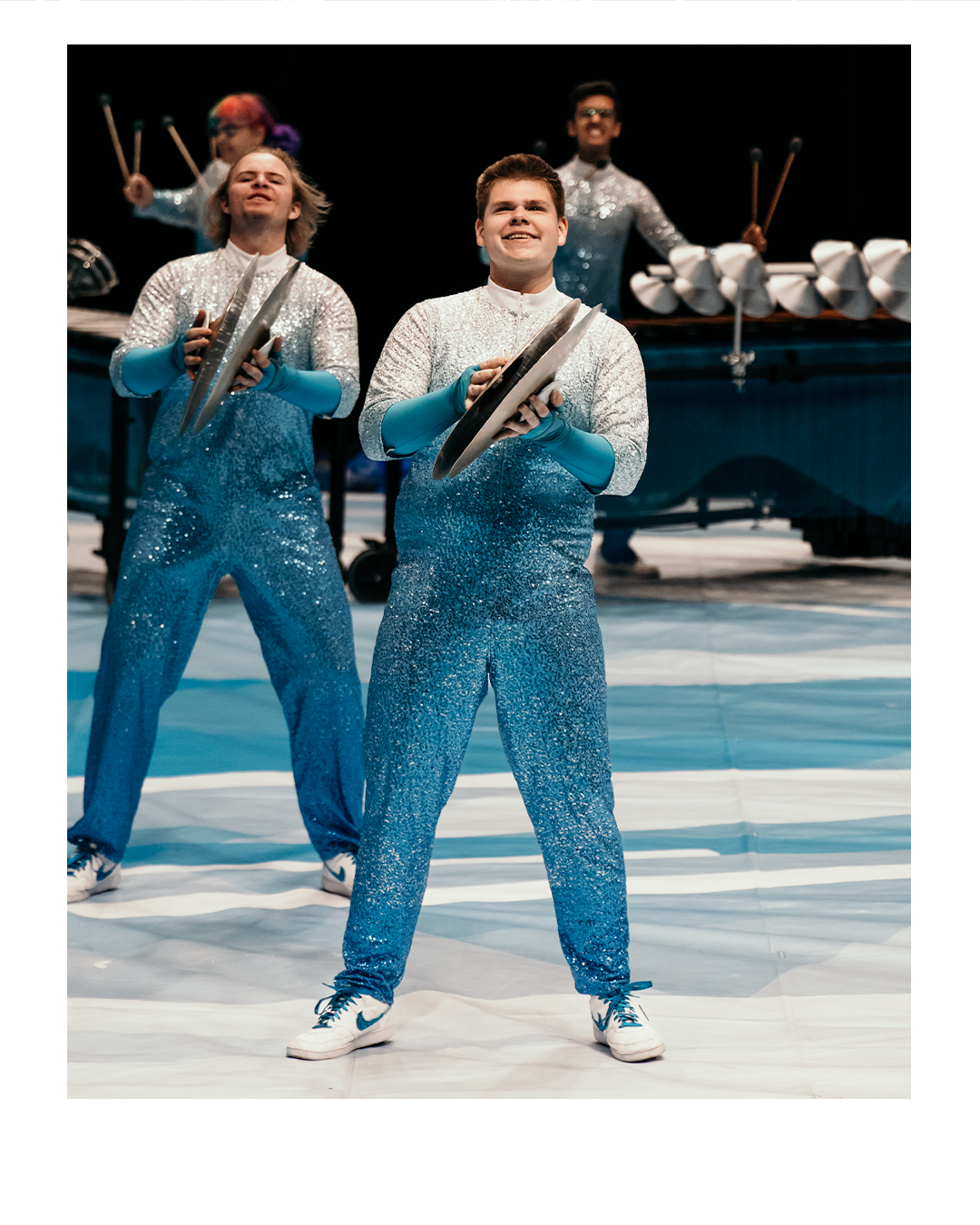 Four young performers in glittery blue costumes holding cymbals during a stage performance.