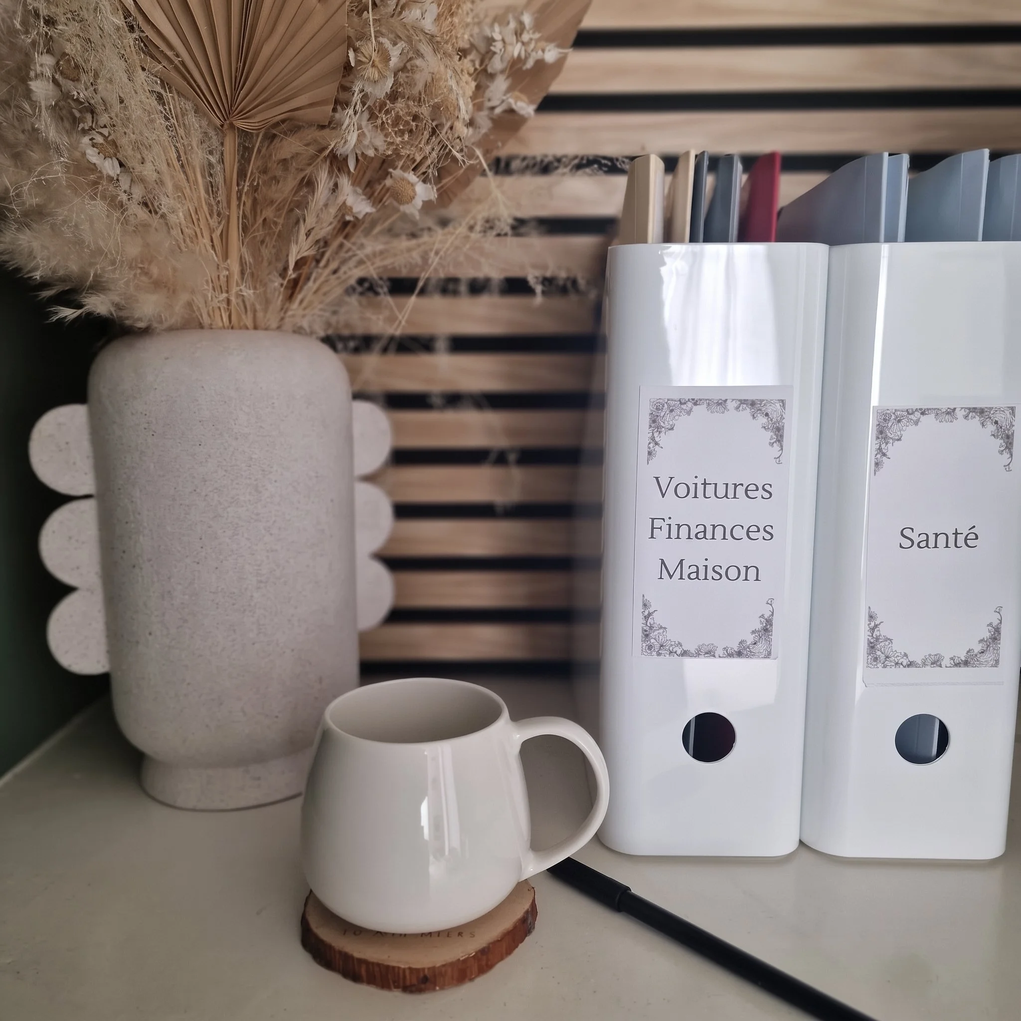 Une étagère avec des livres, des tasses en céramique, et une décoration en fleurs séchées. La photo est prise de côté avec un fond en bois.