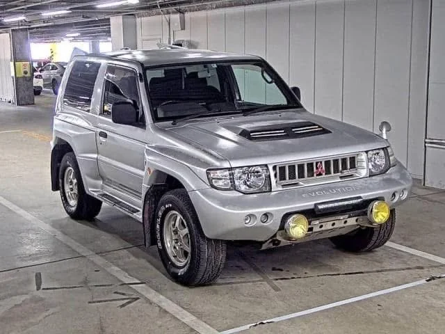 Silver Suzuki SUV with yellow fog lights parked in an indoor garage.