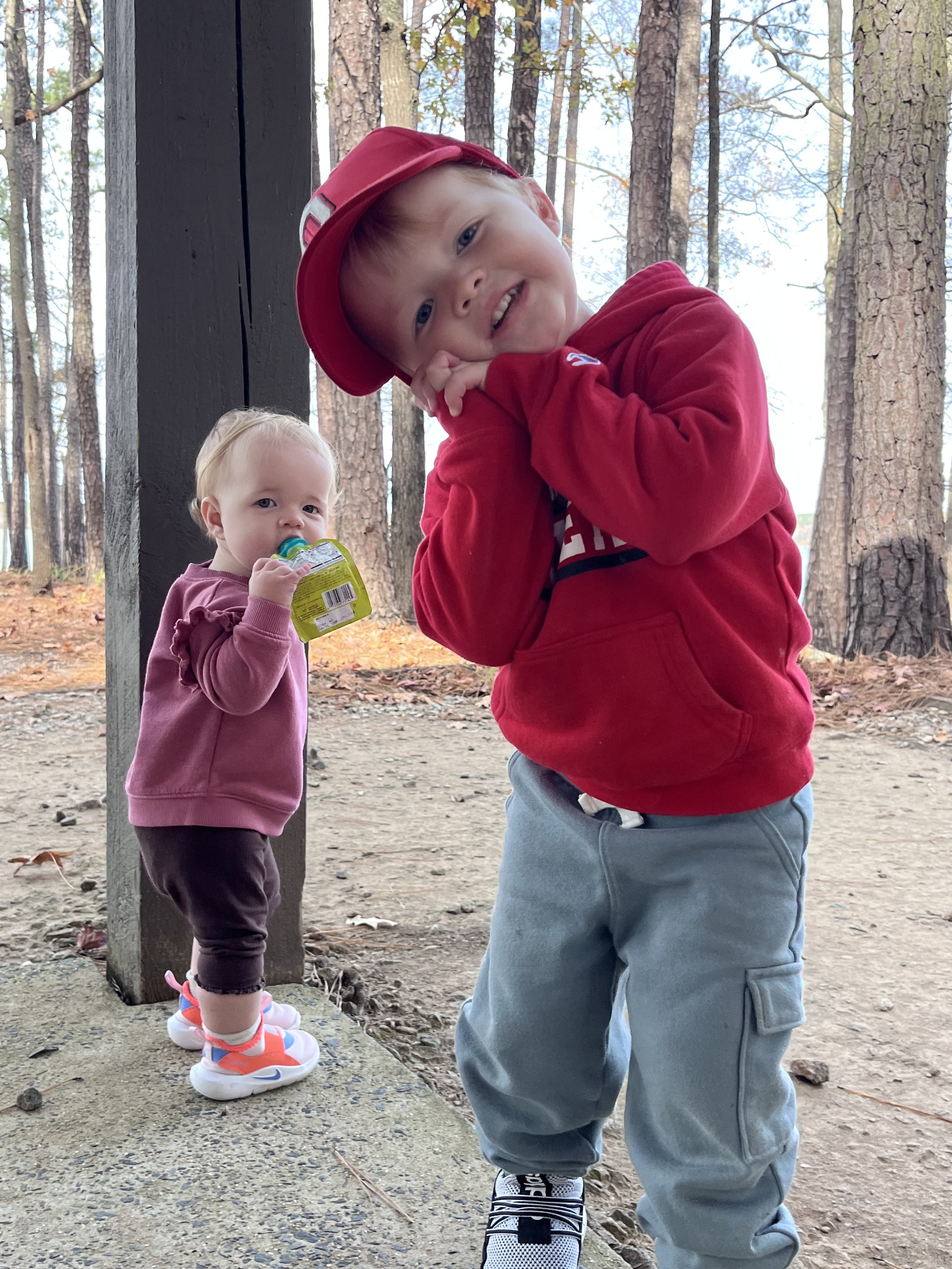 Two young children, a boy and a girl, standing outdoors in a forest.