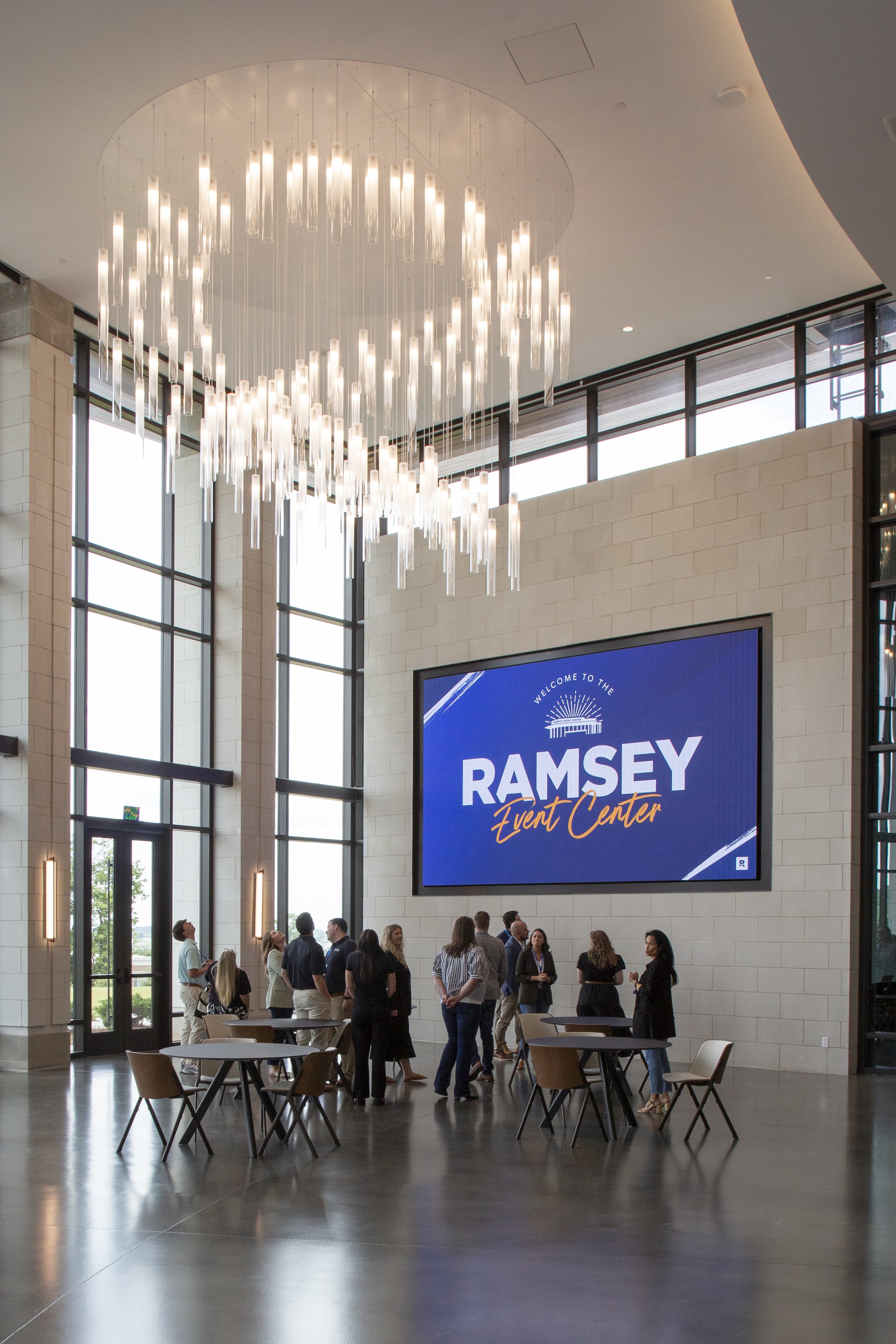 Lobby of the Ramsey Event Center with a large digital screen and a group of people chatting.