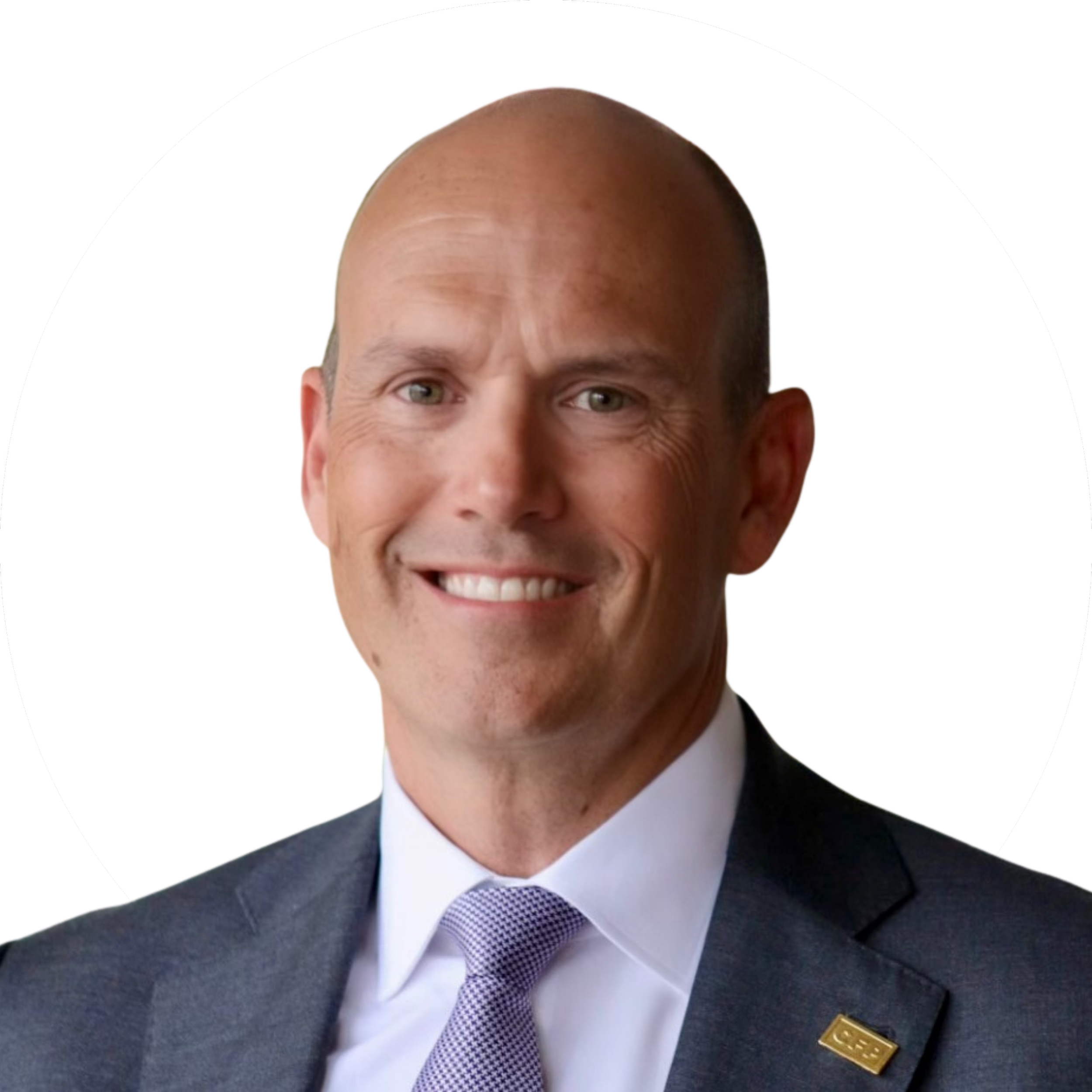 A man in a business suit smiling, with a white shirt, light purple tie, and a pin on his jacket lapel, against a white background with a black circle framing his head.