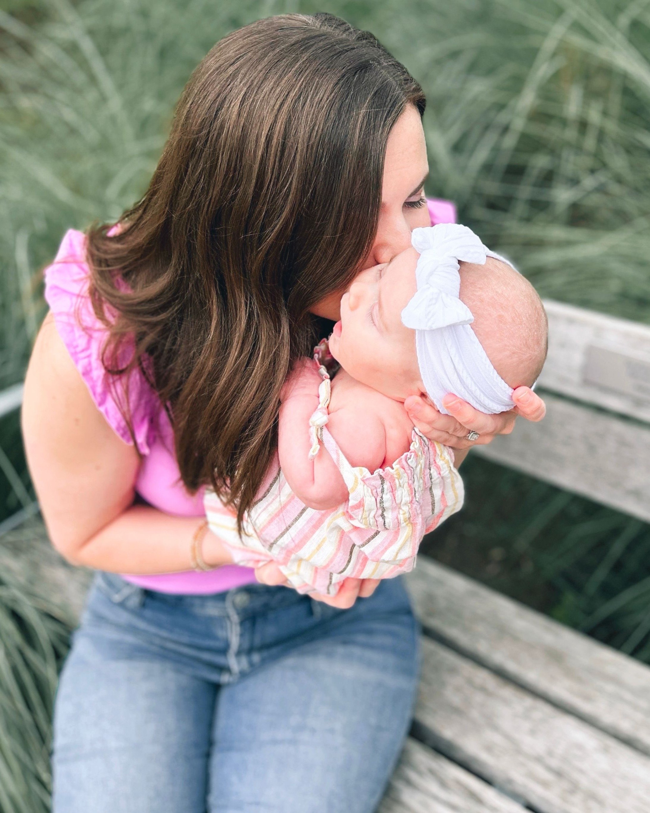 Woman holding and kissing a baby girl on a park bench