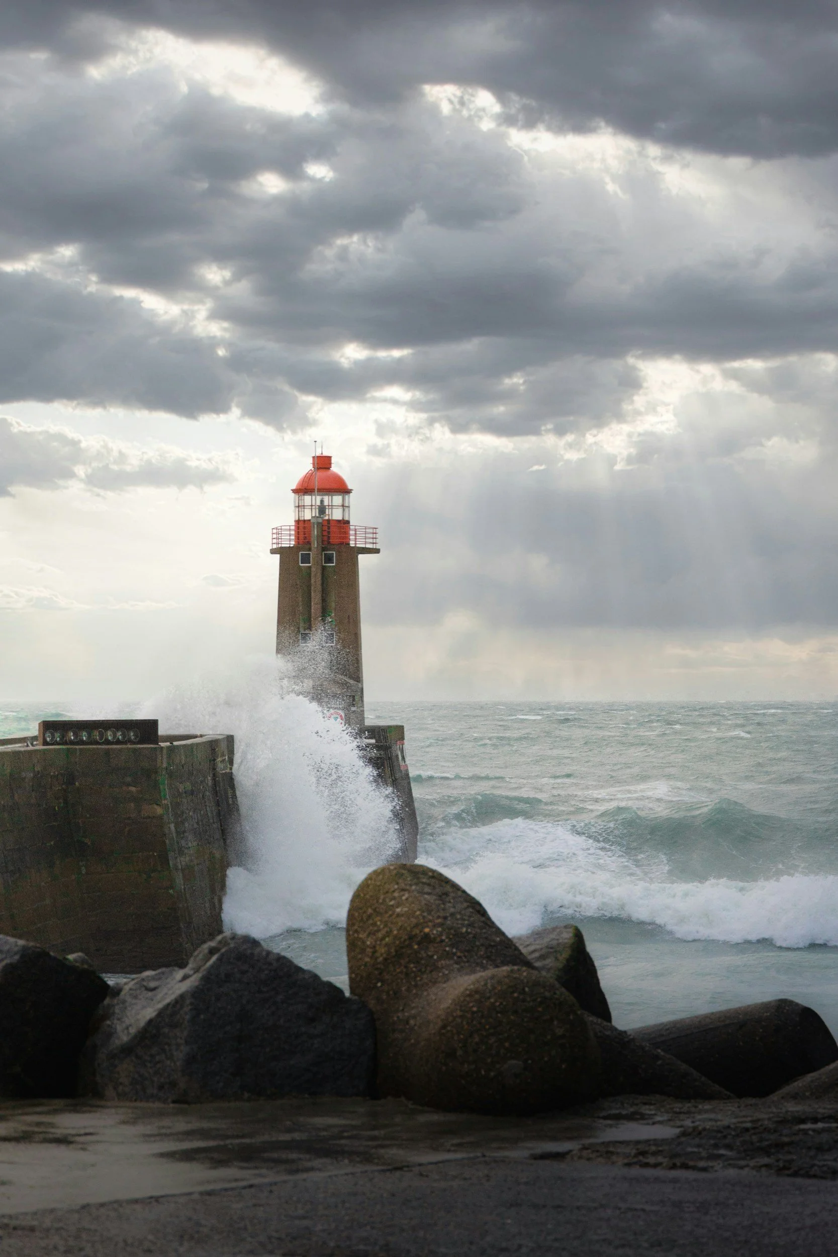 Lighthouse on a rocky shoreline with stormy clouds overhead, waves crashing against the rocks.