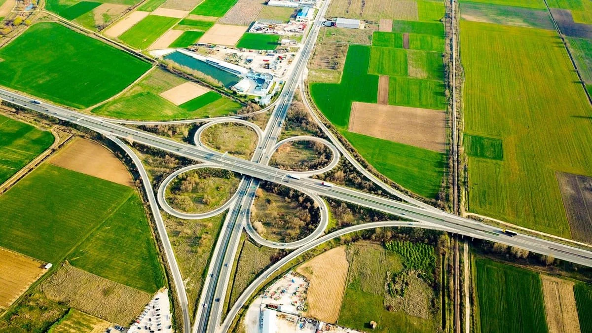 Aerial view of a highway interchange with multiple overpasses and loops surrounded by green and brown fields.