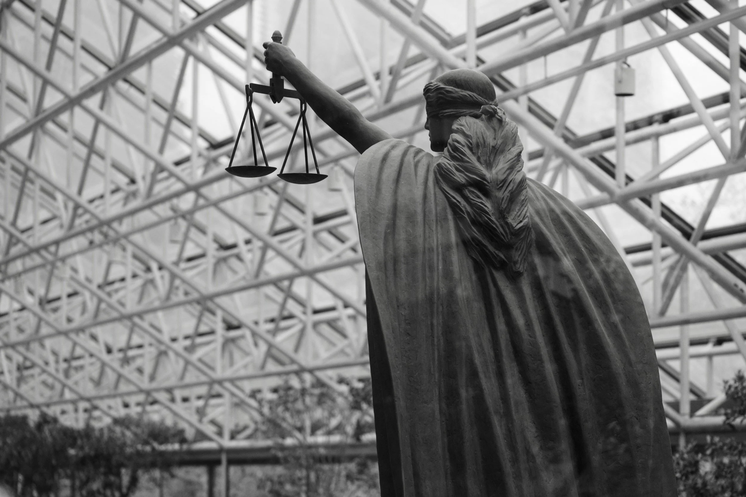 Statue of Lady Justice with blindfold, holding scales, in front of a modern architectural structure