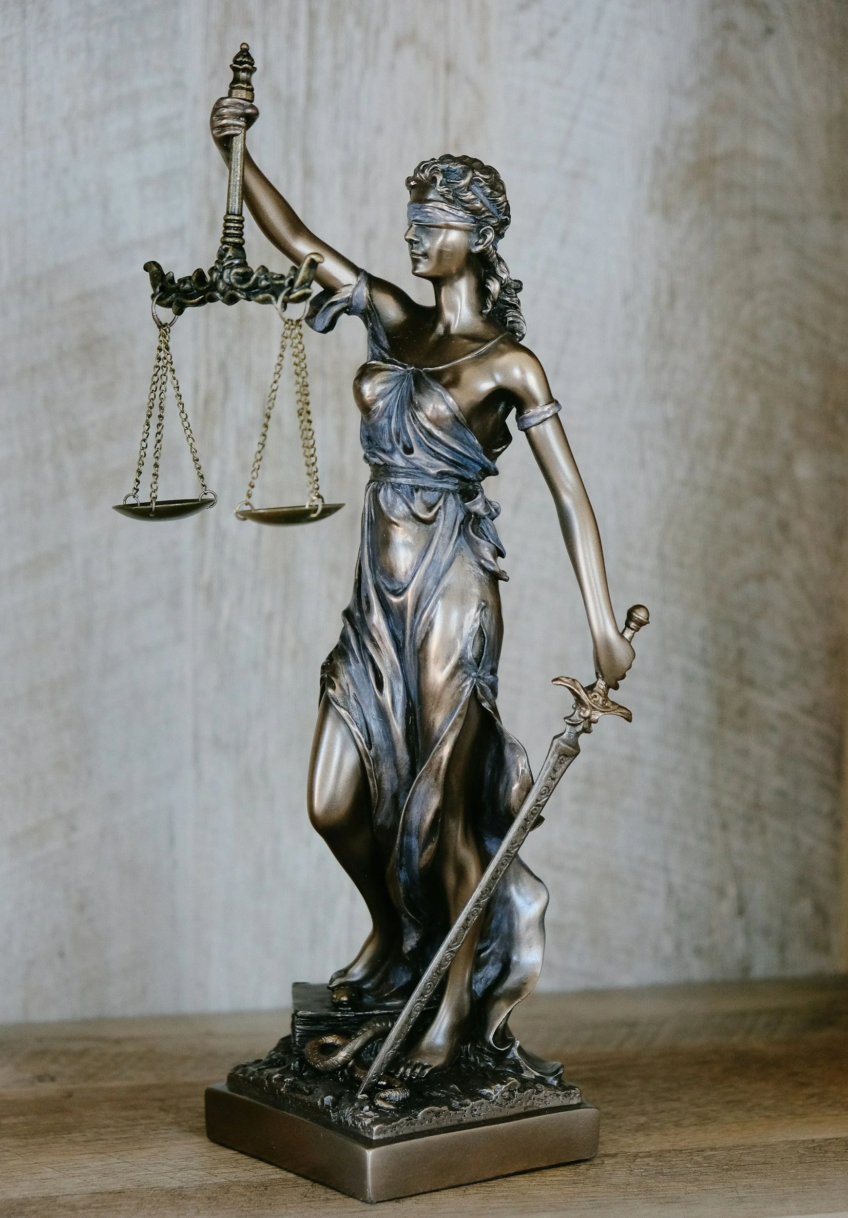 Statue of Lady Justice with a blindfold, holding scales in one hand and a sword in the other, standing on a base.