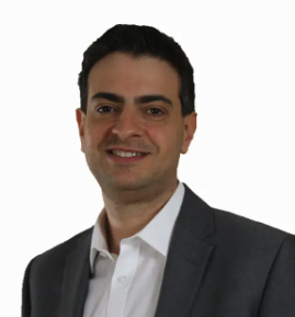 A man with short dark hair and light skin, wearing a gray suit and white dress shirt, smiling against a white background.