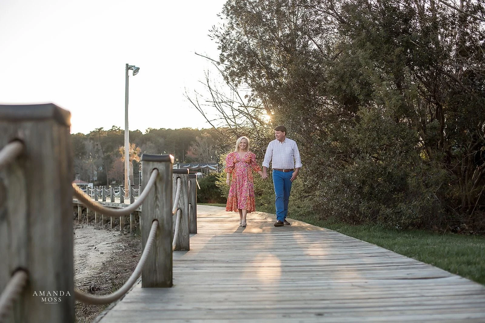 mature couple holds hands and walks towards the camera on a dock at lake norman