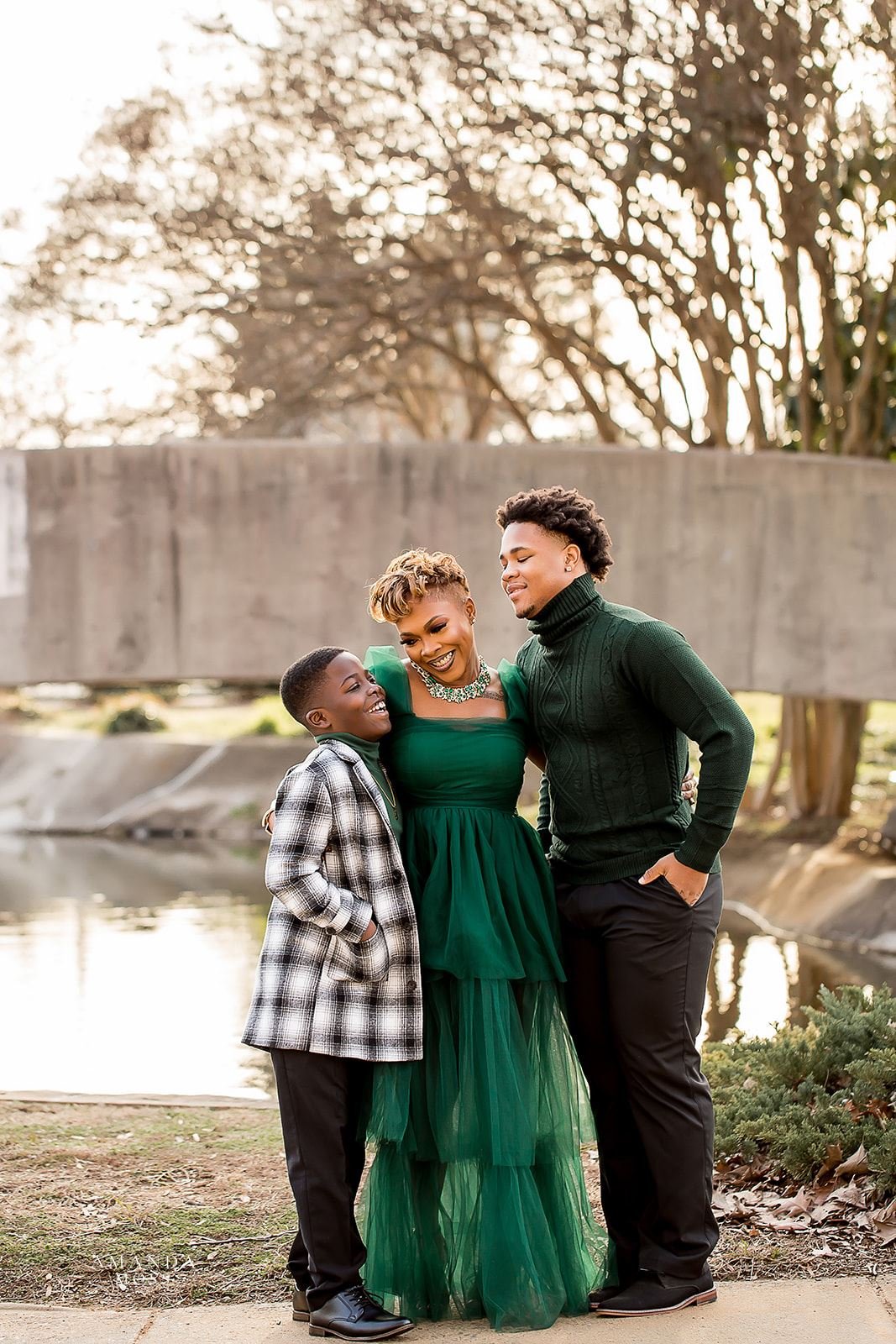 mother in emerald dress embraces her two sons in editorial family shoot at marshall park in charlotte north carolina