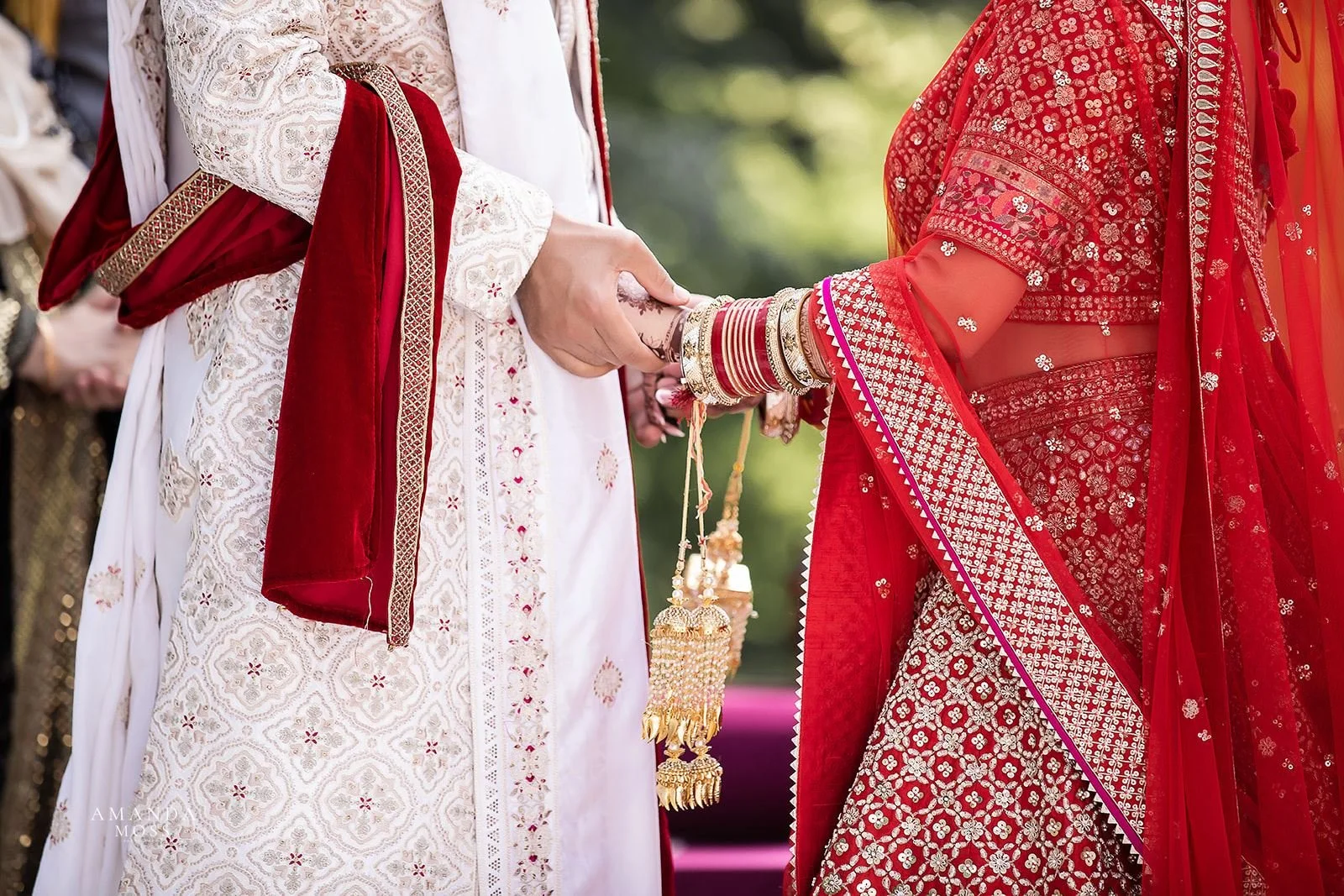 bride and groom hold hands in indian wedding ceremony colors of red, white and gold