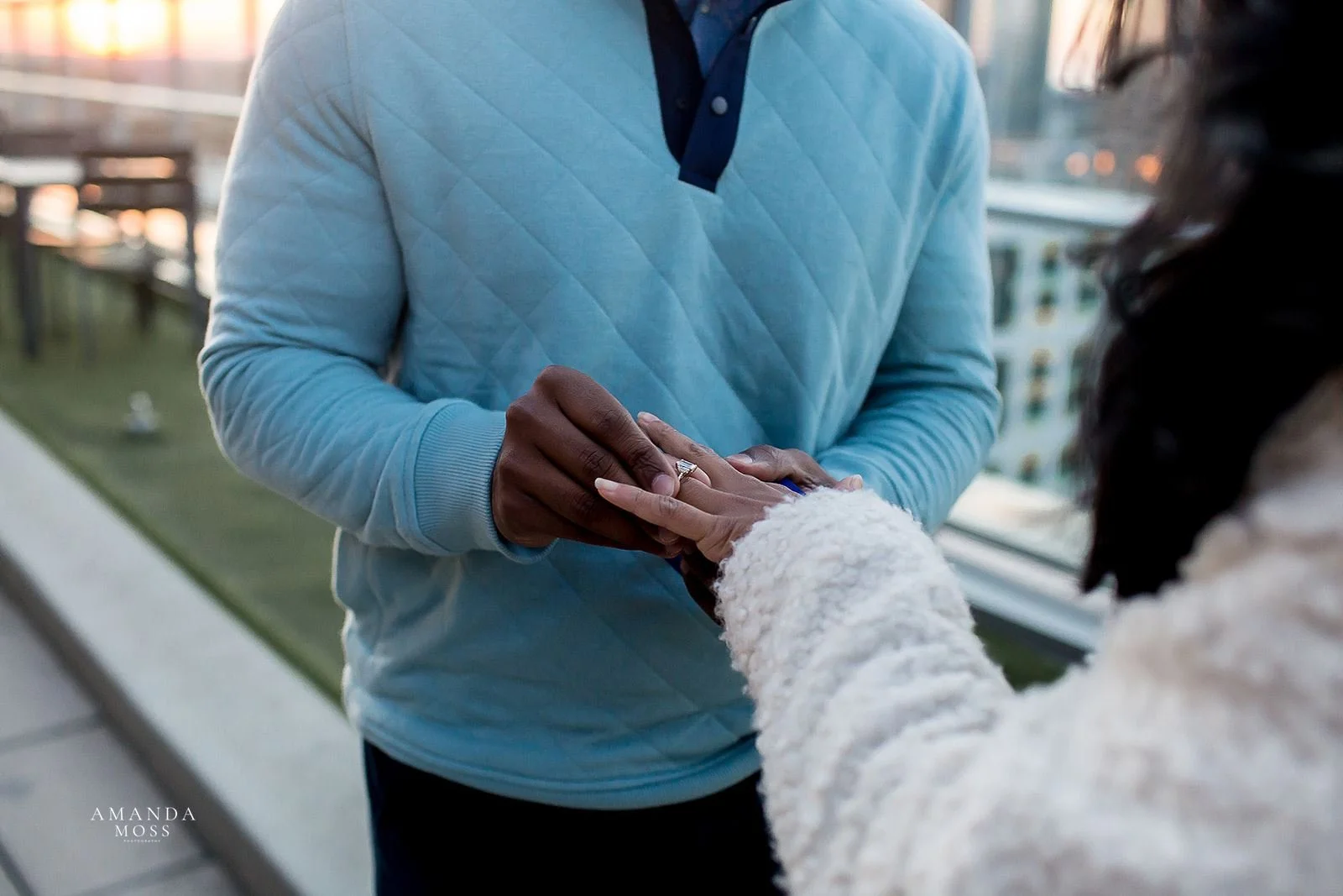 man in blue sweater slides engagement ring onto womans hand