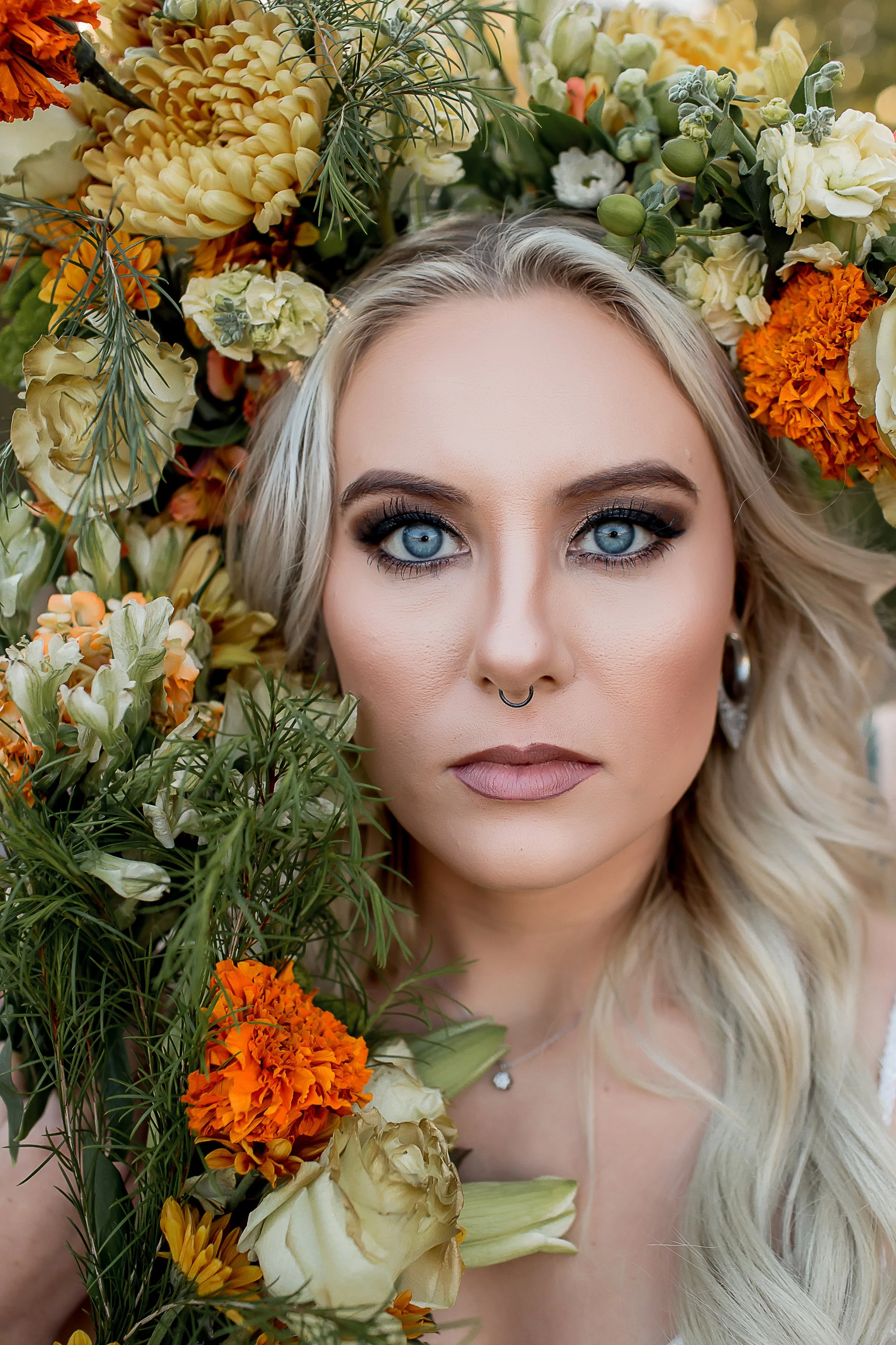 alternative bride with nose piercing and striking blue eyes looks directly into camera with flowers surrounding her head