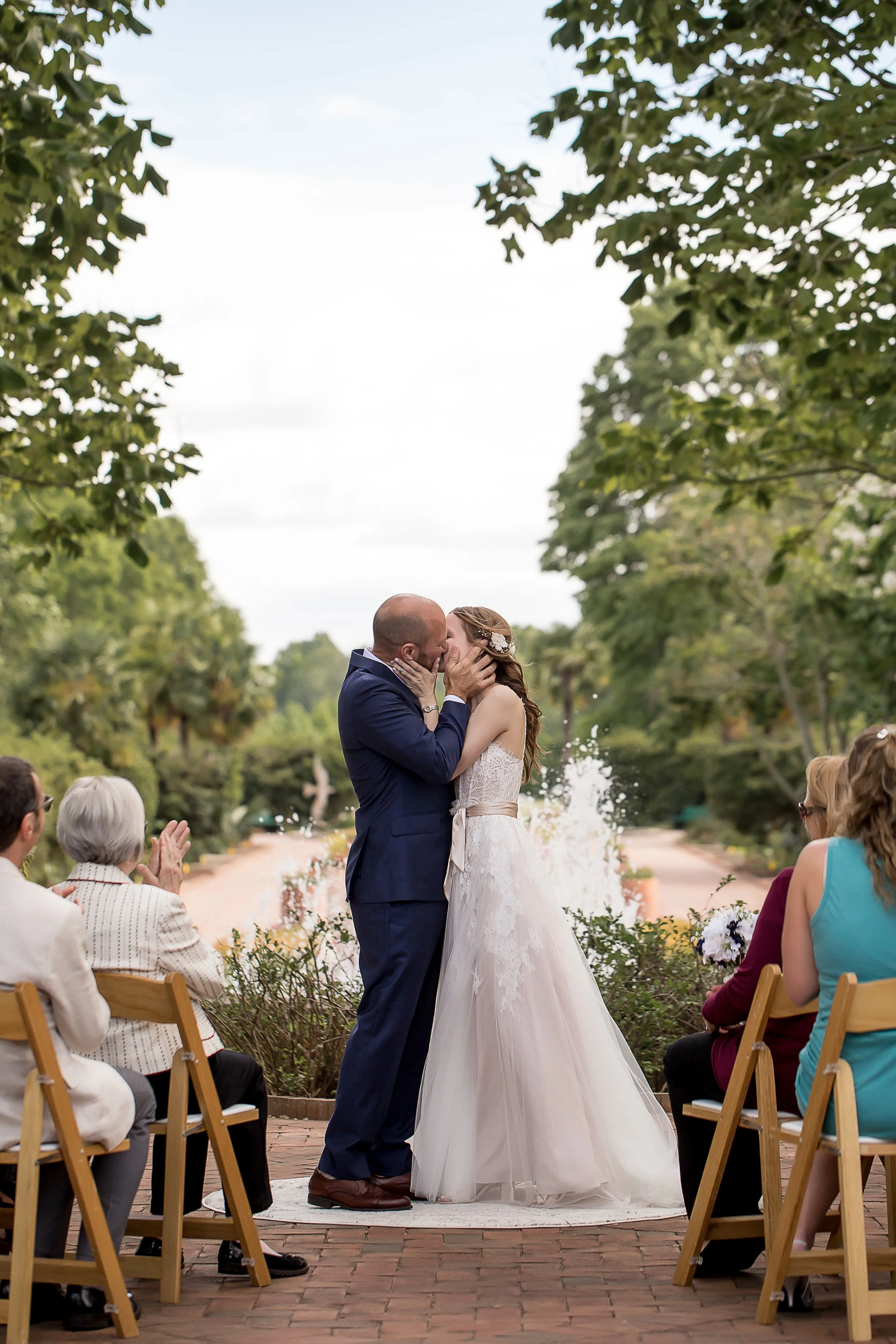 couple embraces with kiss at wedding ceremony in botanical garden