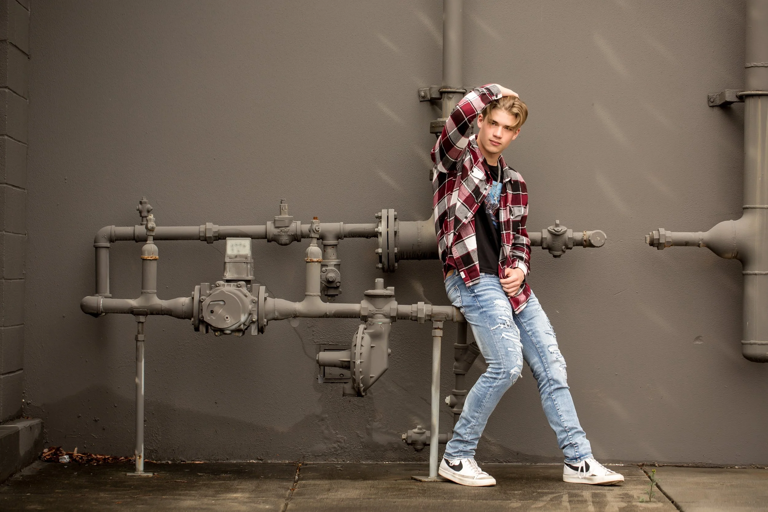 high school senior male in plaid shirt and jeans sits casually on water pipes