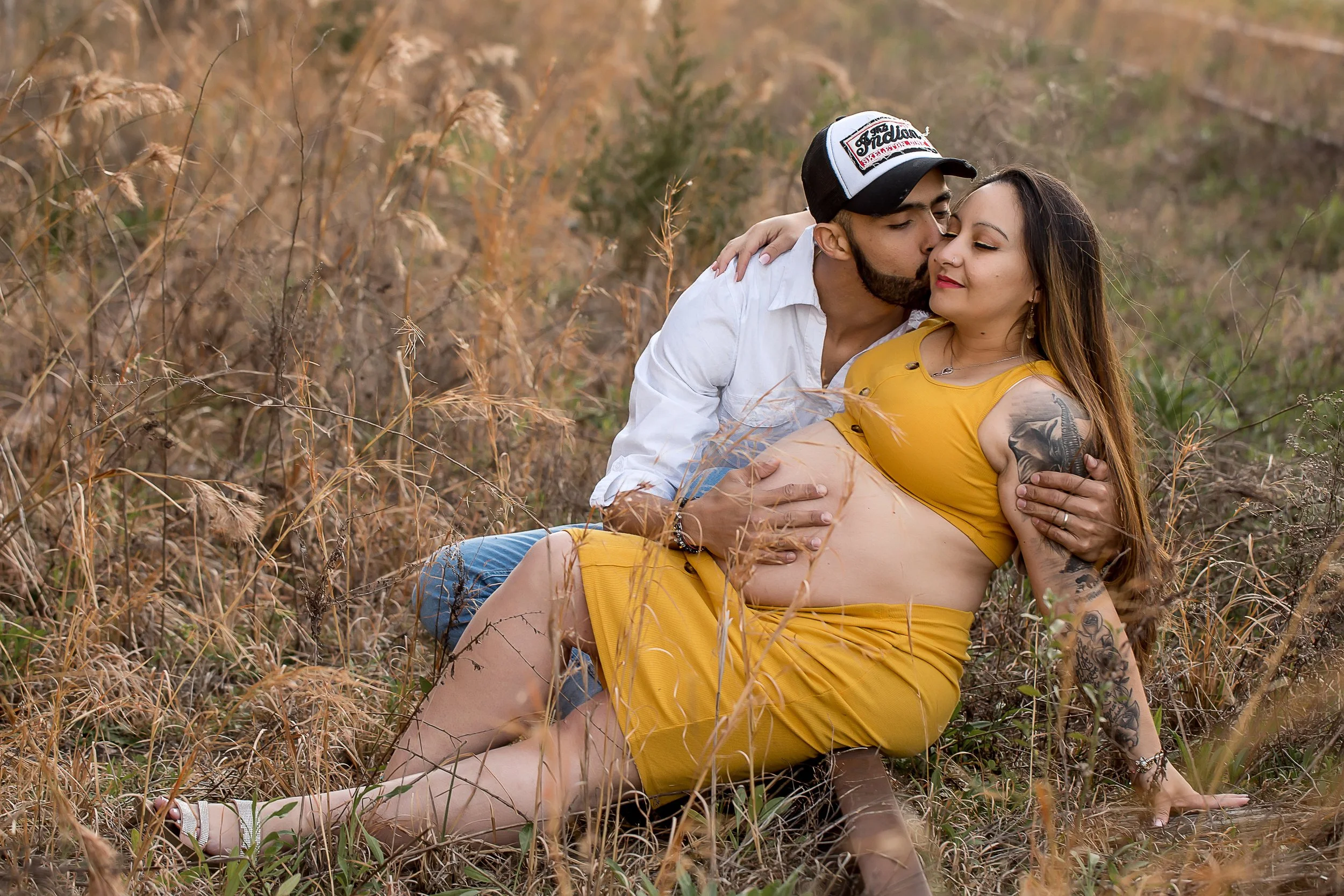 tattooed latin pregnant couple embrace in tall yellow grass