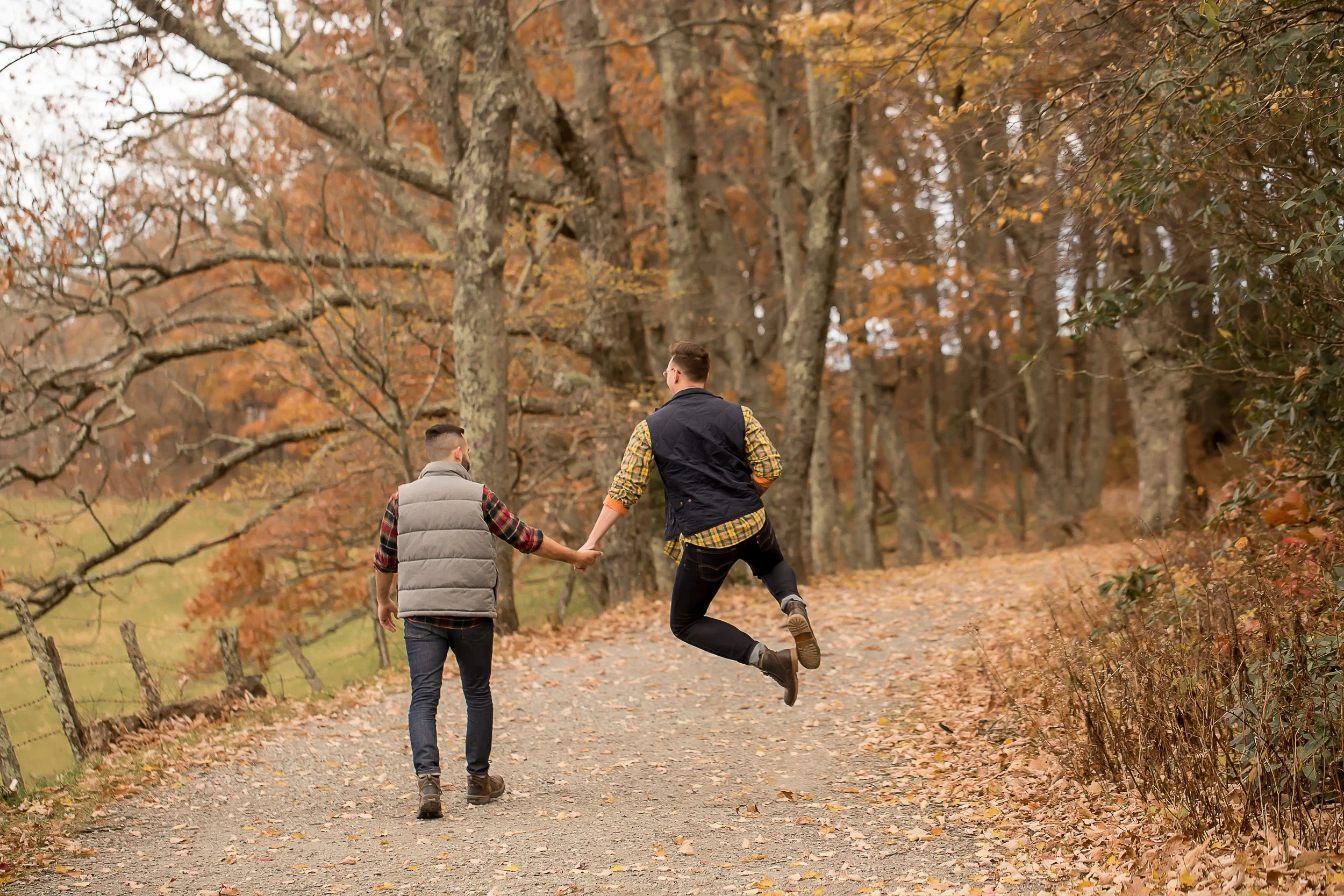 lgbt gay couple walk away from the camera hand in hand while one jumps in the air touching his heels together