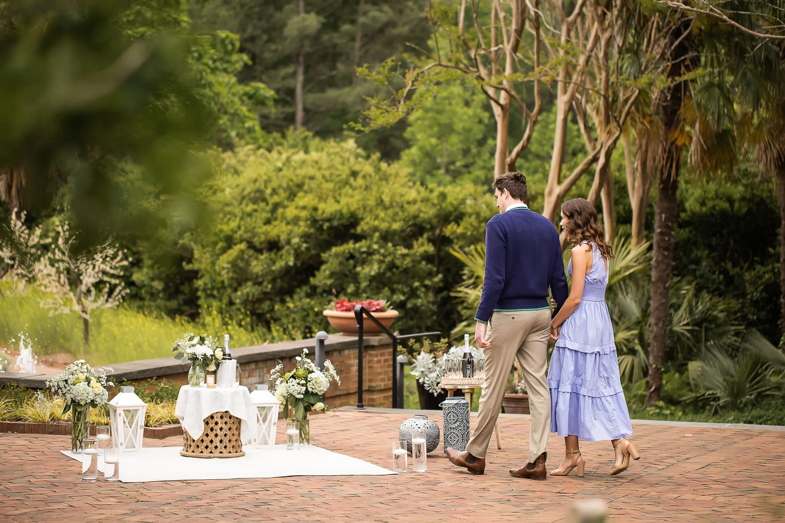 couple dressed in blue walking to a surprise picnic for a proposal at daniel stowe botanical garden