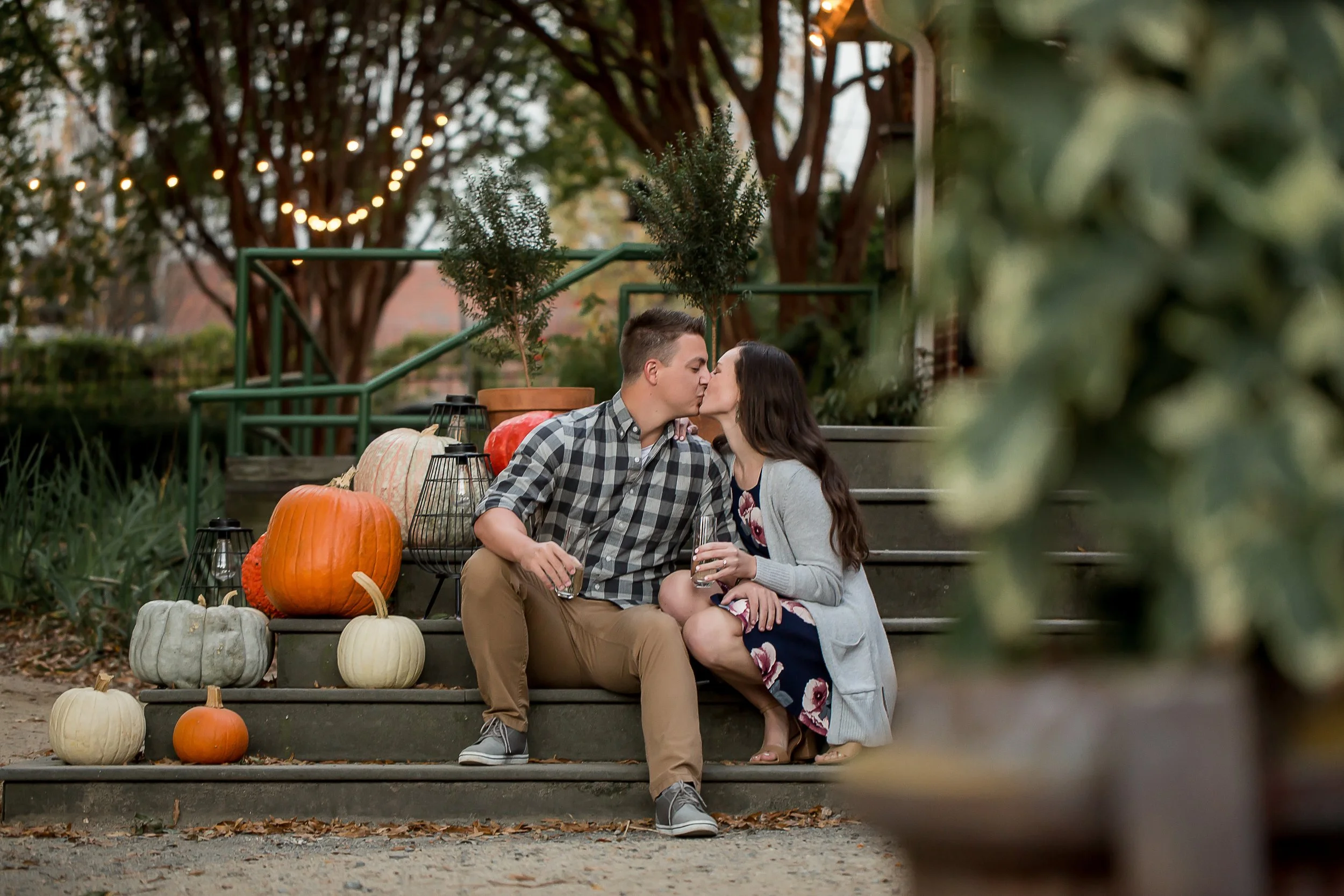 fall photo of newly engaged couple celebrating with champagne on a porch decorated with pumpkins at rosies wine bar in charlotte nc noda neighborhood
