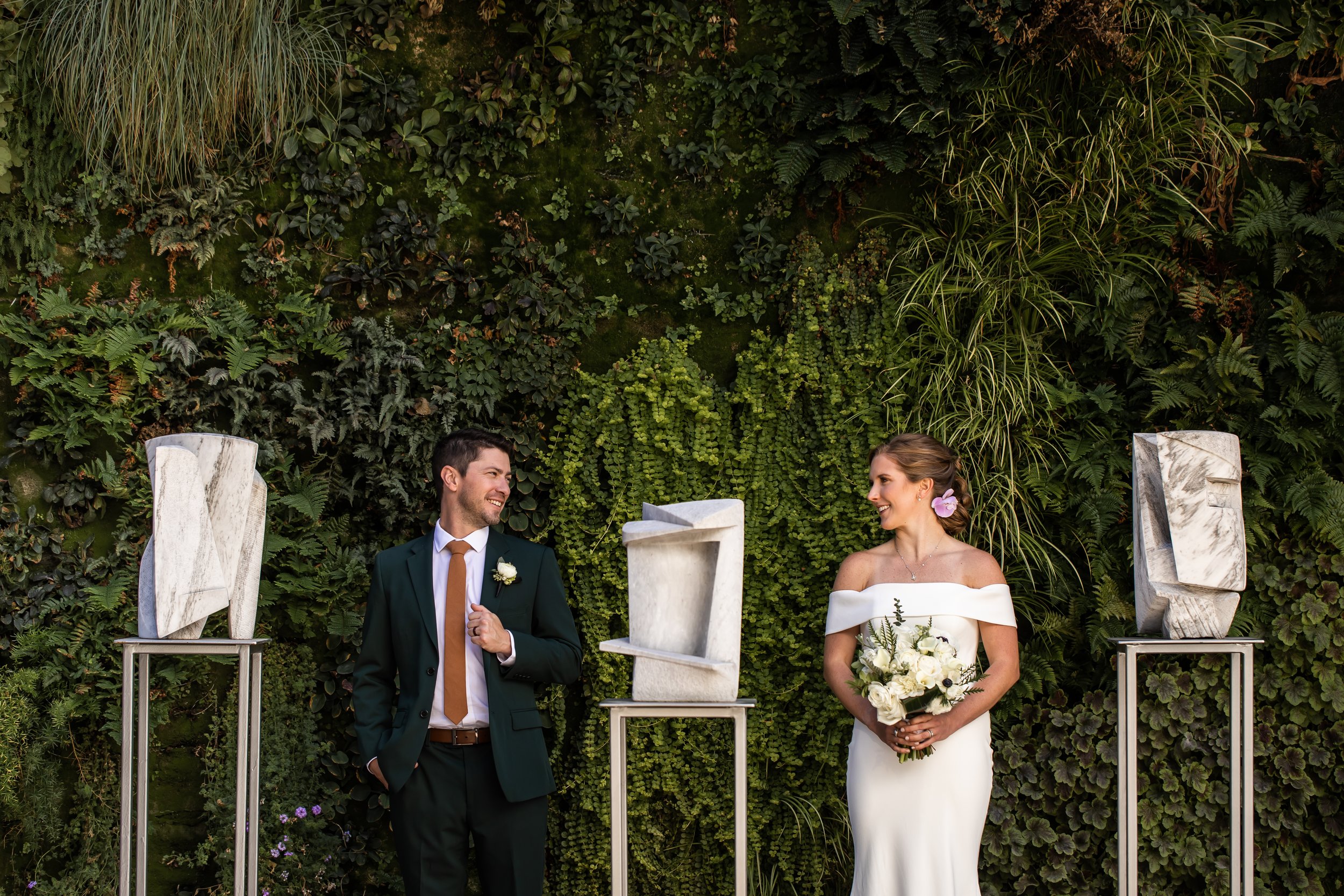 bride and groom look at each other in pose in front of greenery wall fftc charlotte nc uptown micro wedding