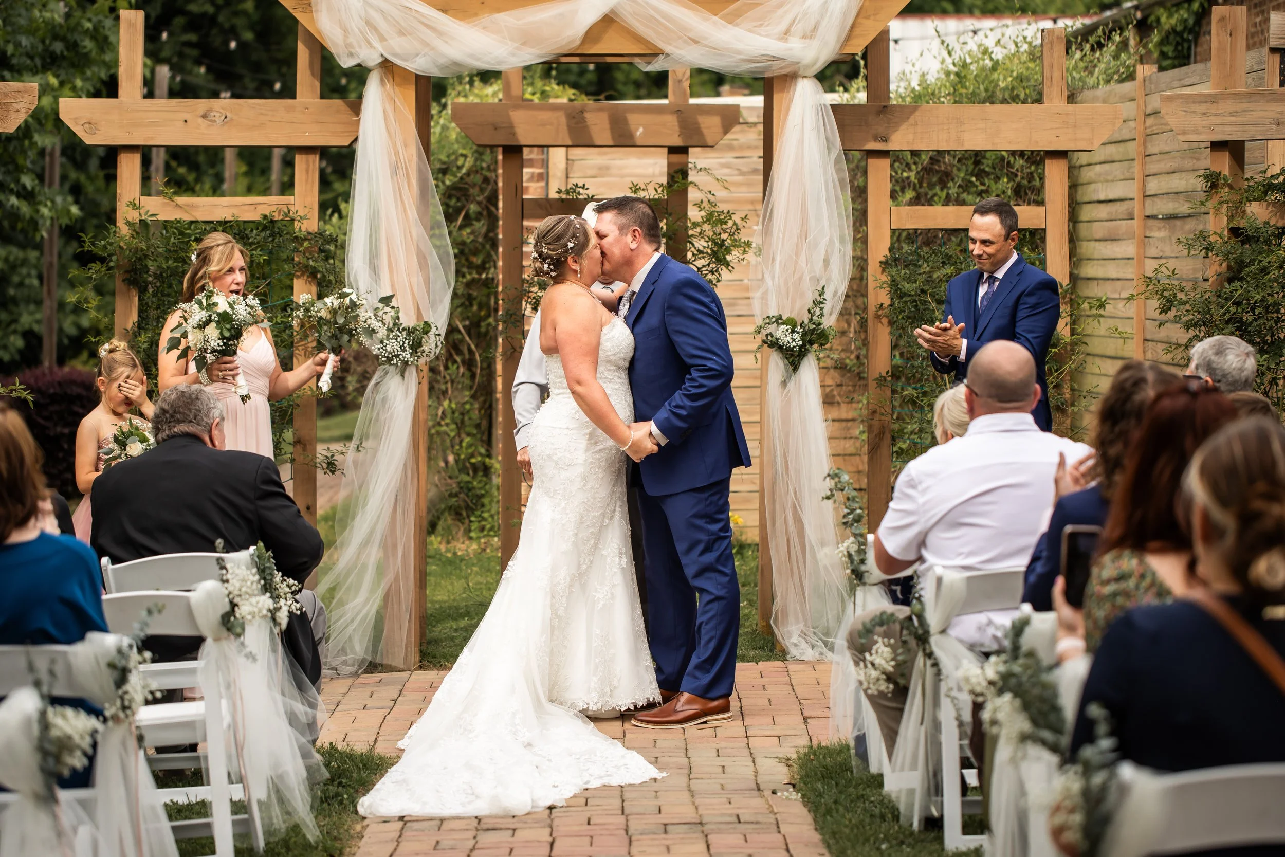 first kiss bride and groom wedding ceremony blue suit outdoor drapery flowers