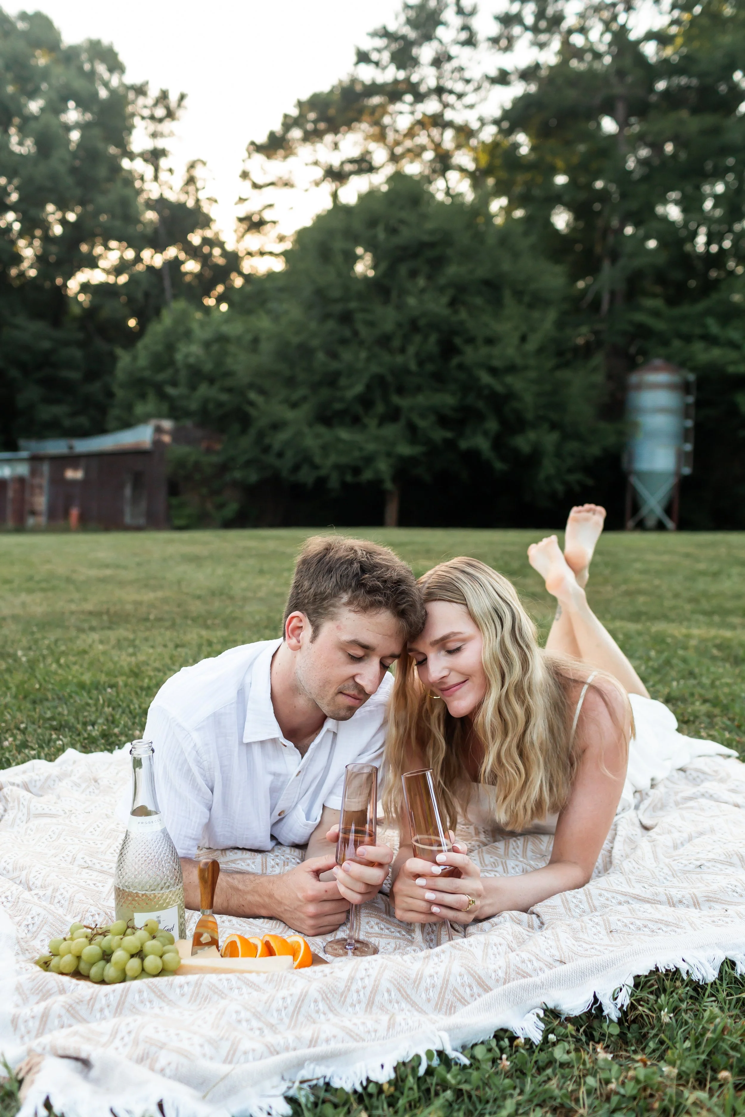 young engaged couple enjoys champagne at a picnic session charlotte nc park